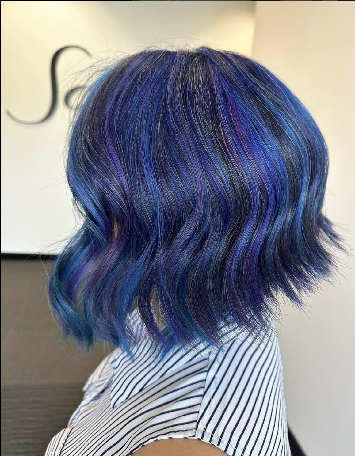 A woman with wavy shoulder-length hair dyed in vibrant shades of blue and purple.