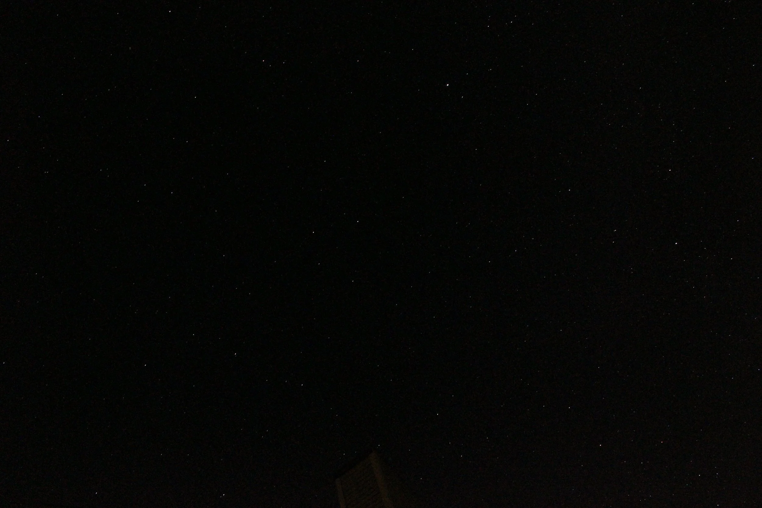 Night sky filled with stars, with a dark silhouette of a building at the bottom.