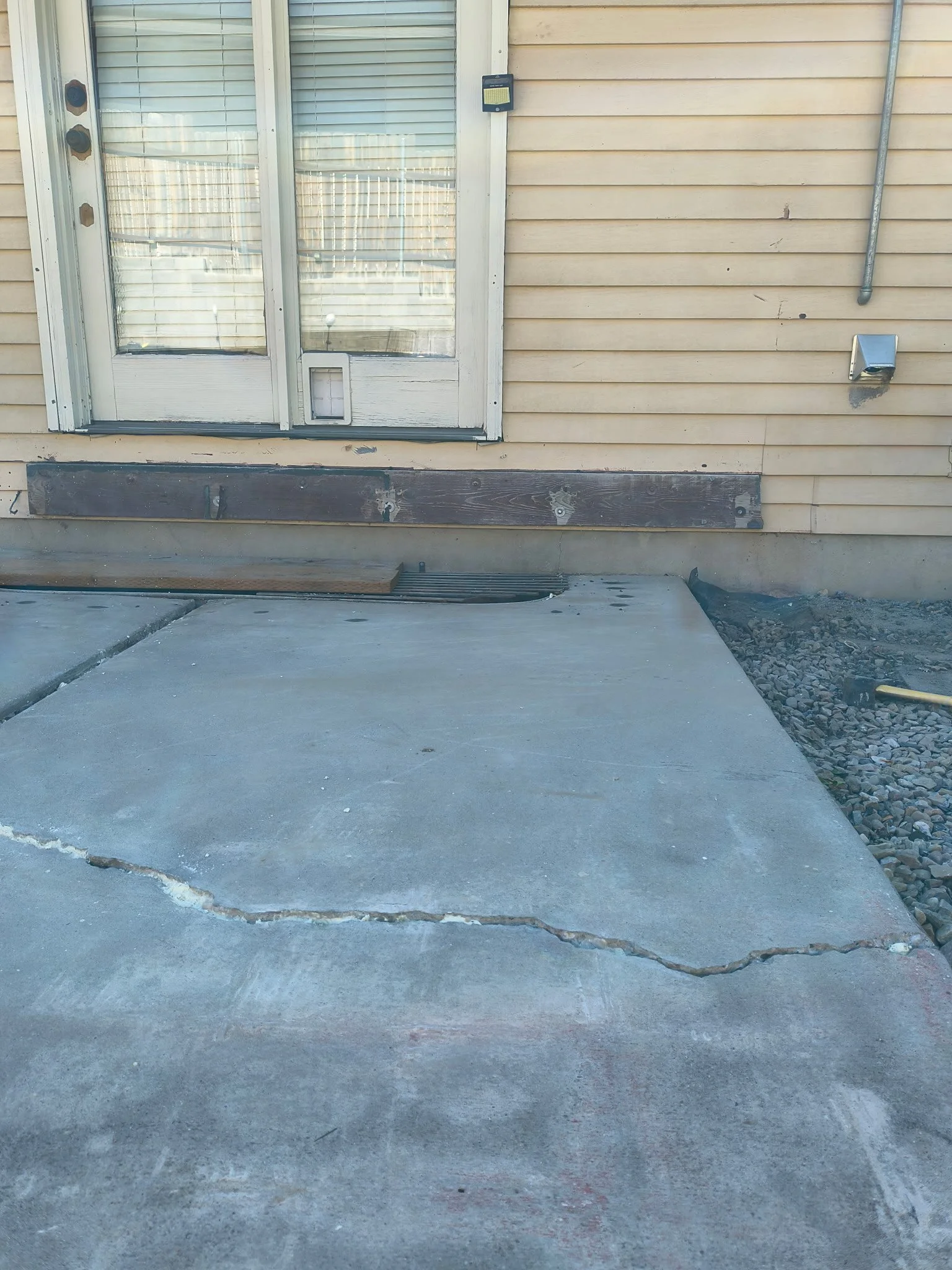 Cracked concrete porch in front of a house with vinyl siding, a sliding door, and electrical fixtures.