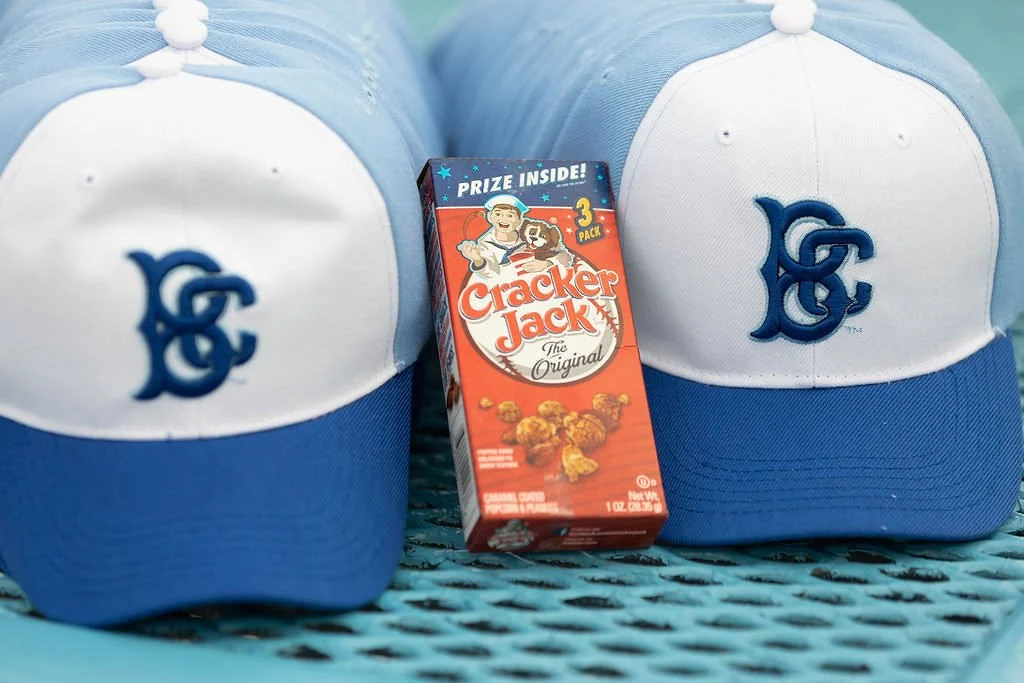 One cracker jack box set between two blue Brooklyn Cyclones hats on a blue metal table, image for a divorce ceremony