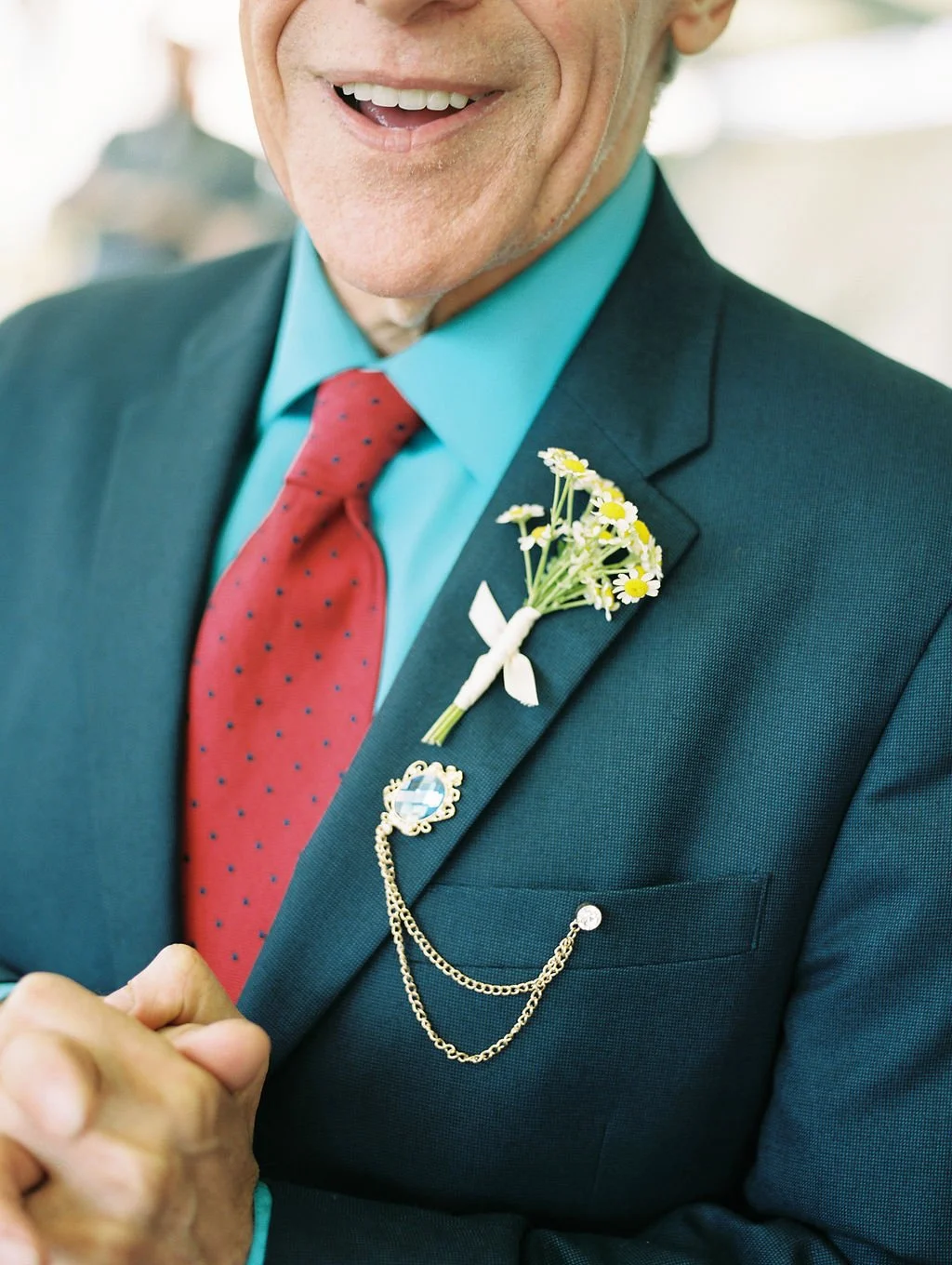 Older white male smiling towards the camera with a teal suit, red polka dot tie and a chamomile bouttoniere, image for a memorial ceremony