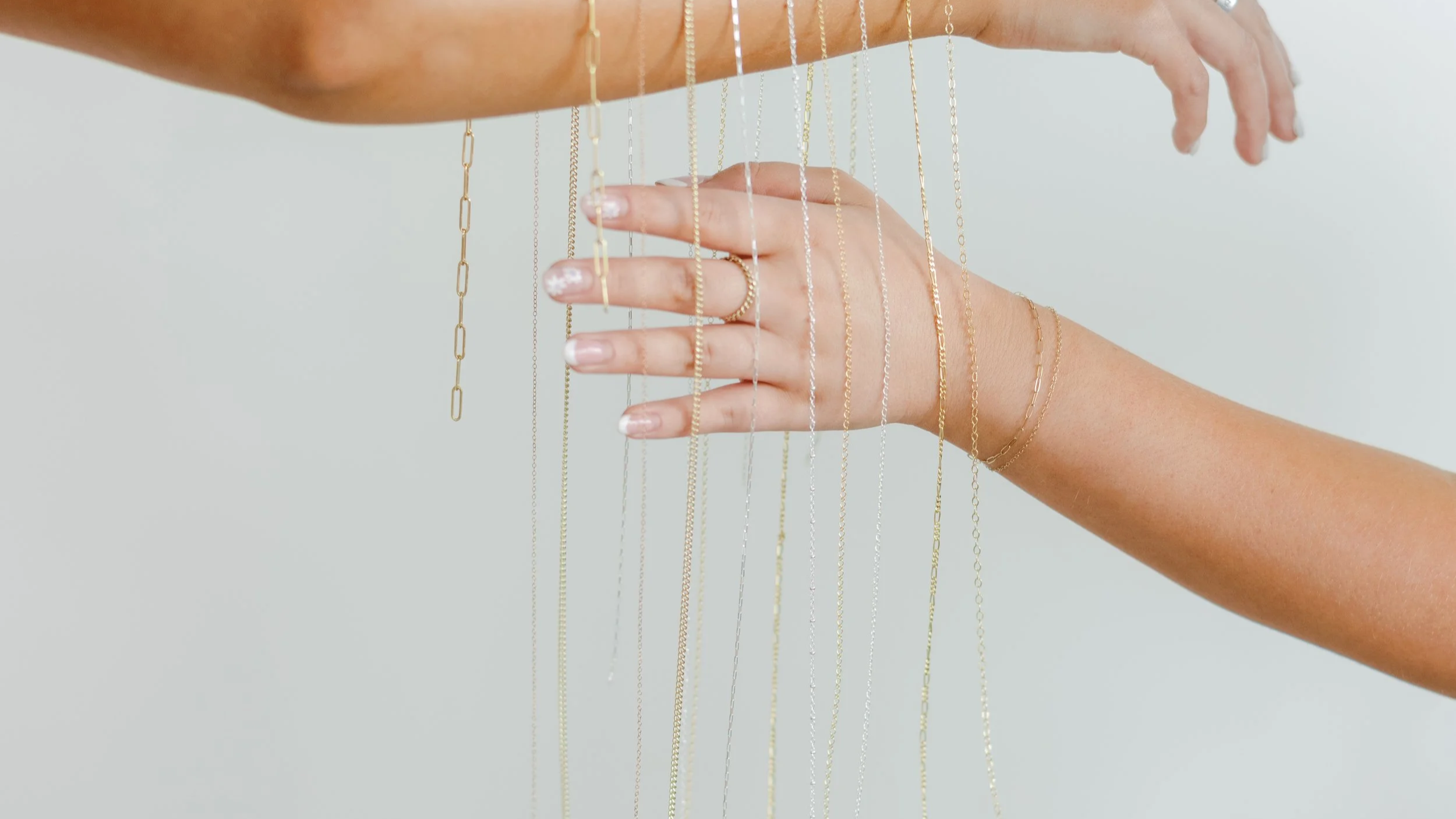 Hands surrounded by hanging gold and silver chains and jewelry.