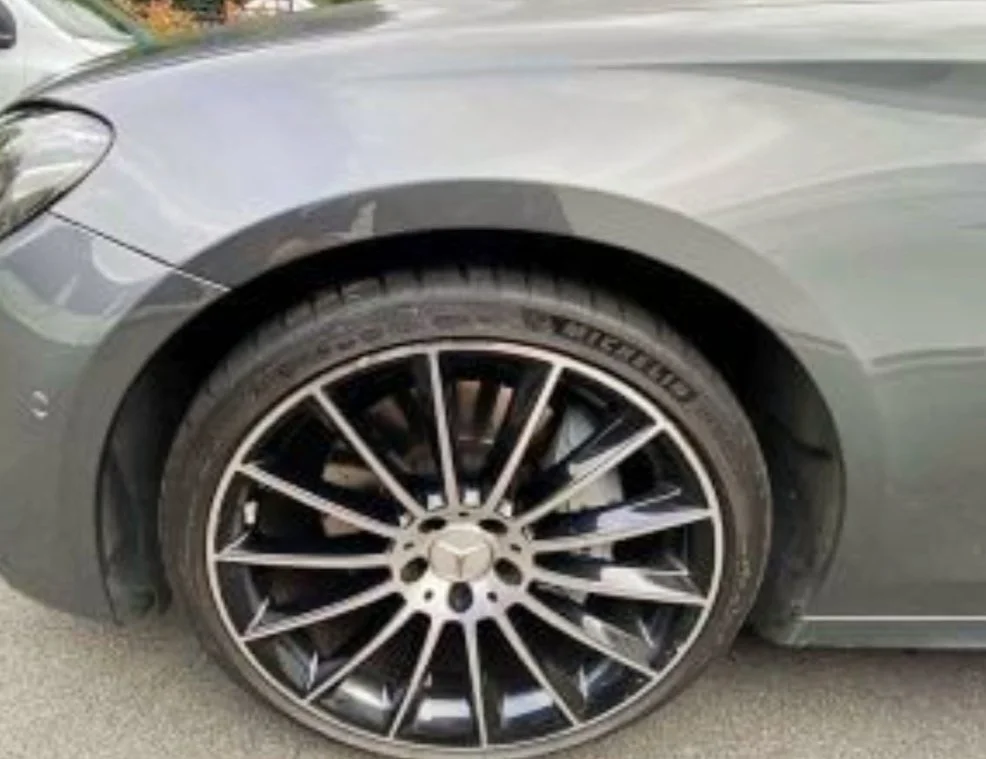 Nahaufnahme des vorderen Rads eines grauen Autos mit schwarzem und silbernem Leichtmetallrad.