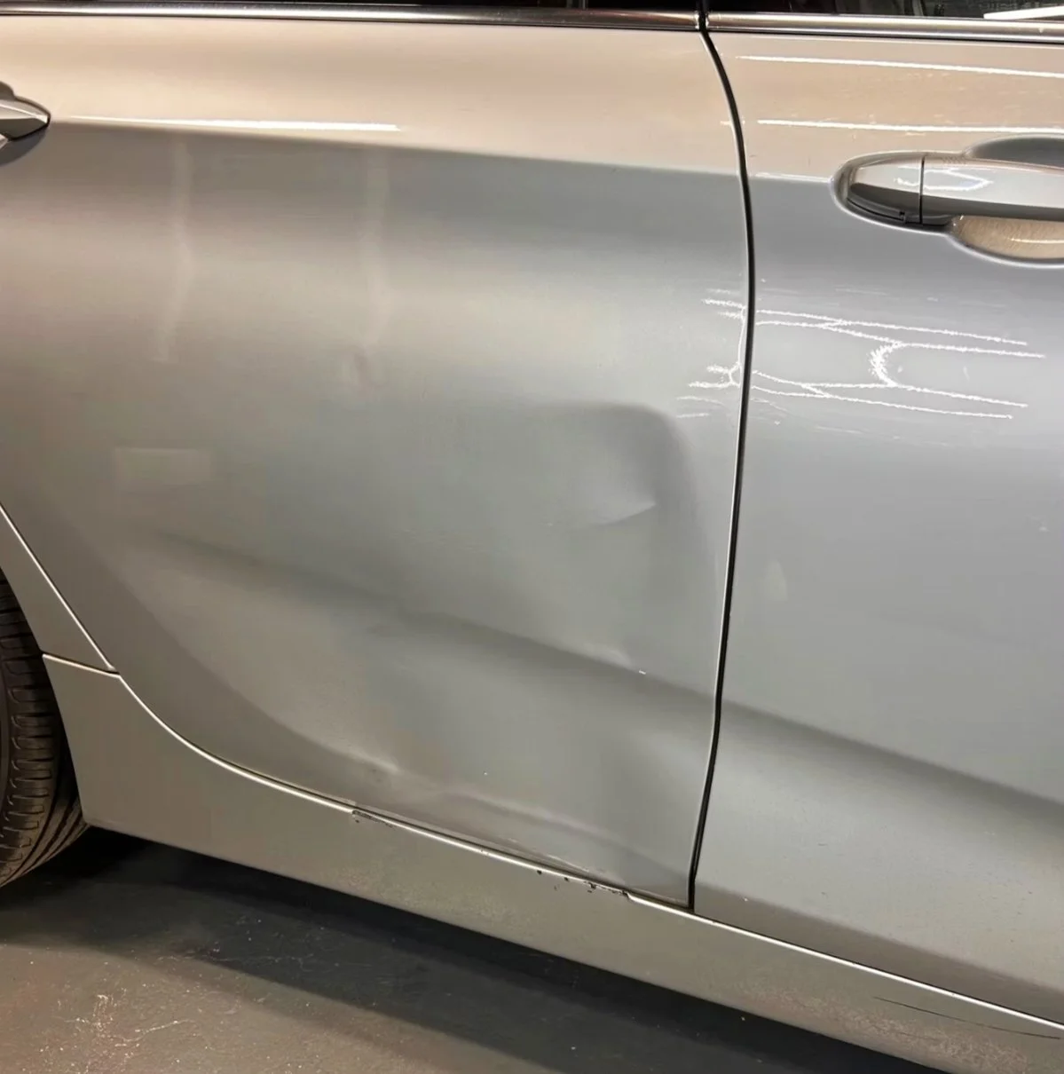 Die Seite eines silbernen Autos mit einem Kratzer am unteren Bereich der Tür.