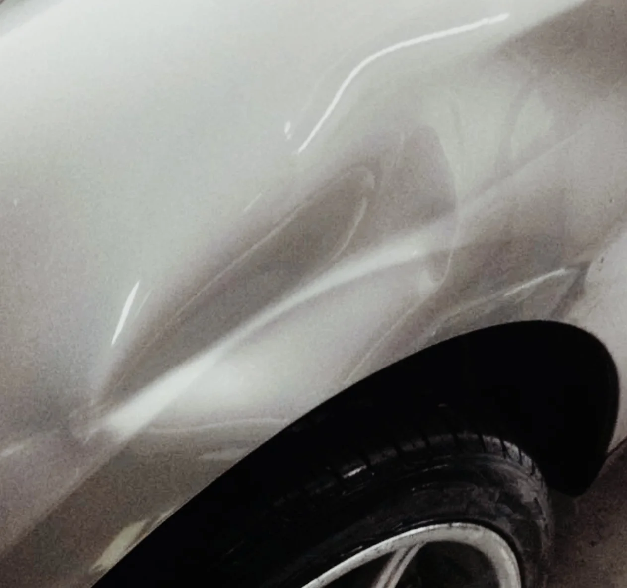 Nahaufnahme eines beschädigten weißen Autos, sichtbarer Kratzer und Delle an der Karosserie, Vorderreifen und Rad