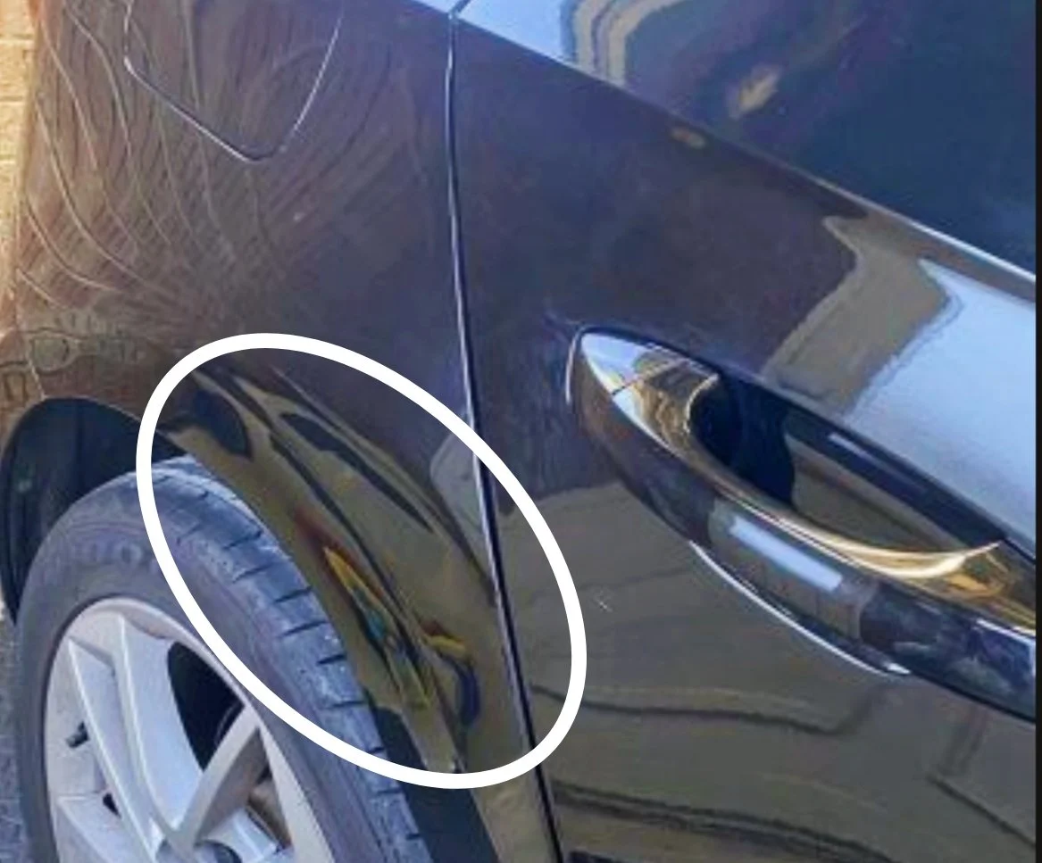 Nahaufnahme eines schwarzen Autos mit einer sichtbaren Beule auf der vorderen Türseite, markiert mit einem weißen Oval.