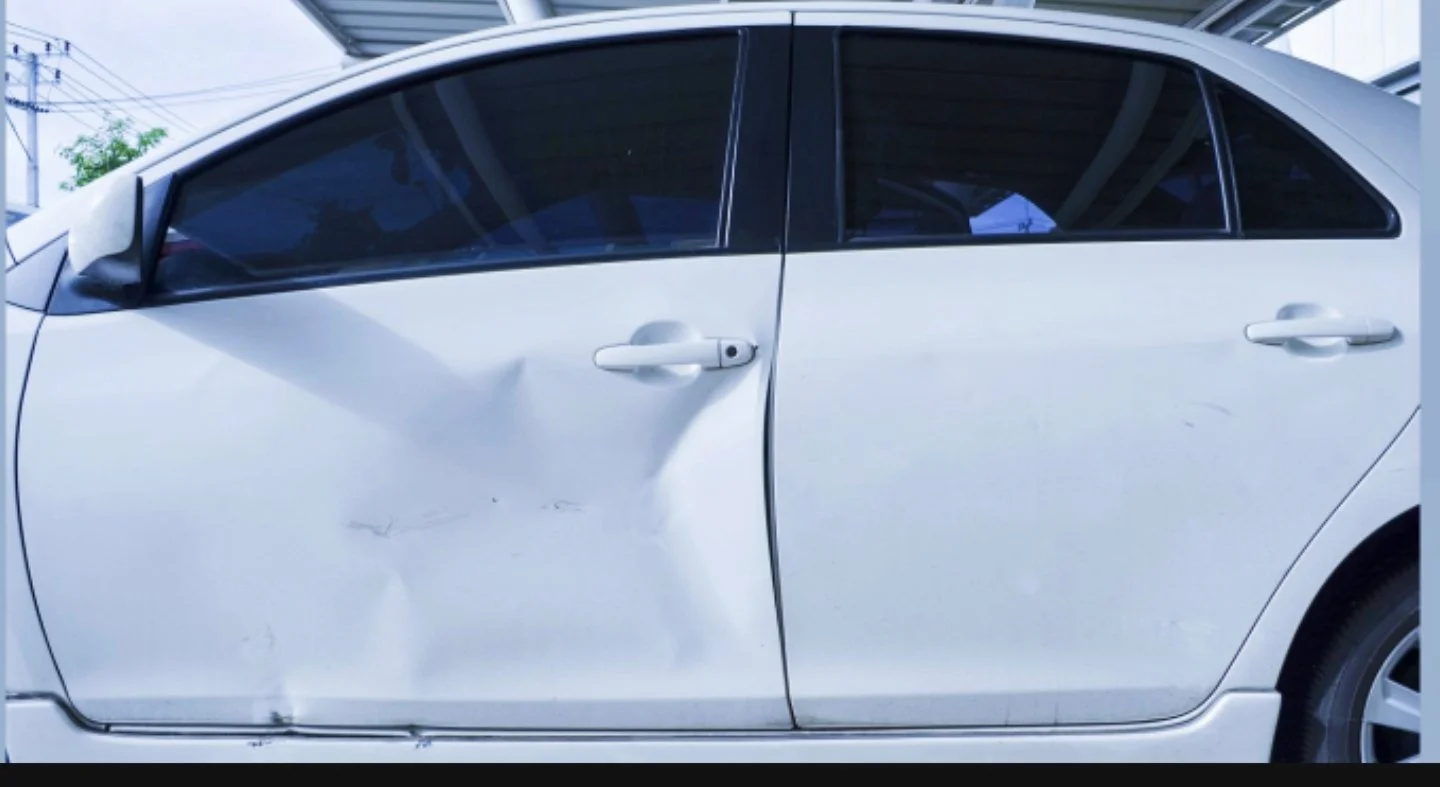 Ein weißes Auto mit sichtbaren Dellen und Kratzern an der Fahrerseite.