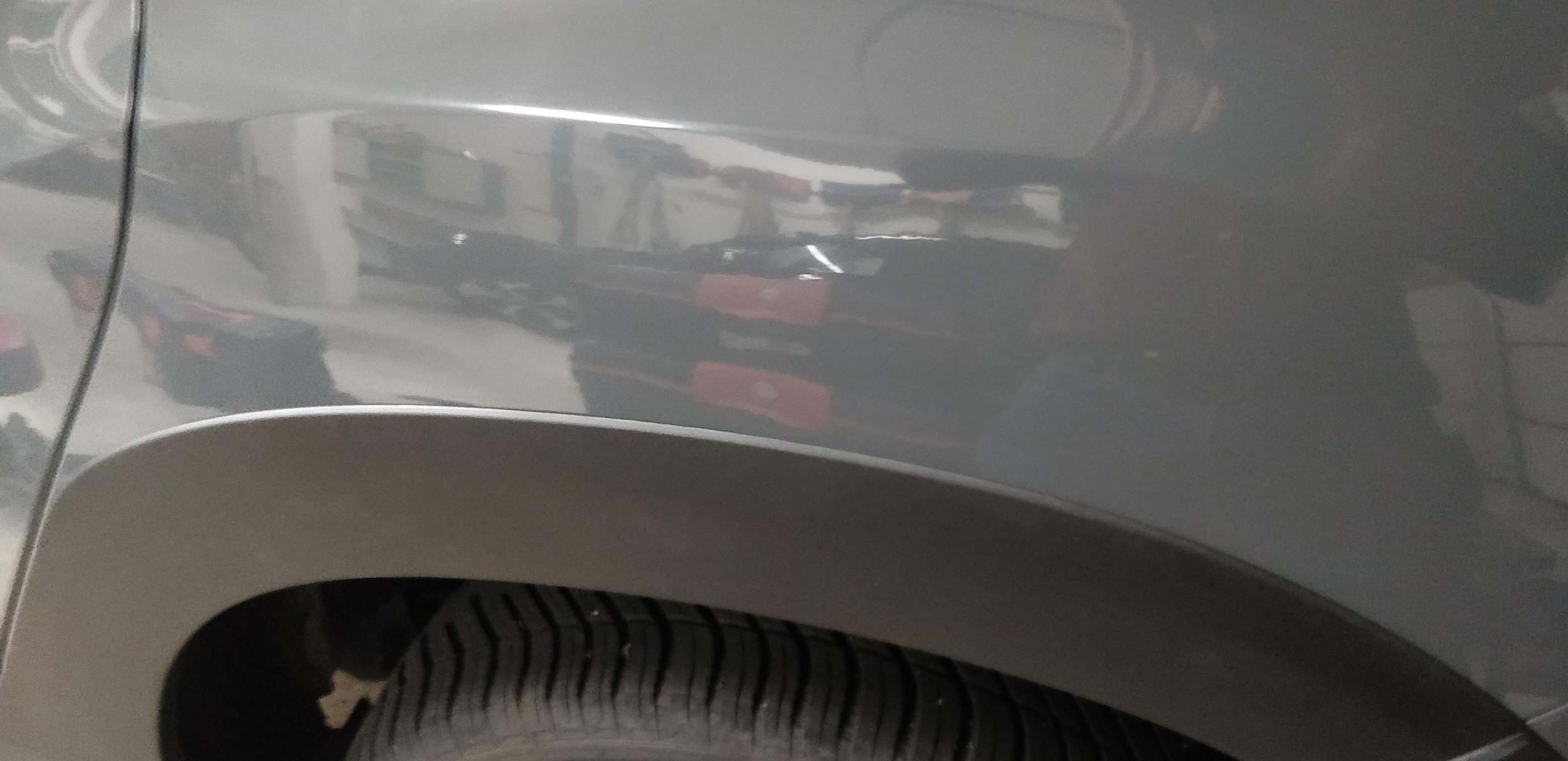 Nahaufnahme eines Autoreifens und der Radlauf eines grauen Autos in einer Werkstatt