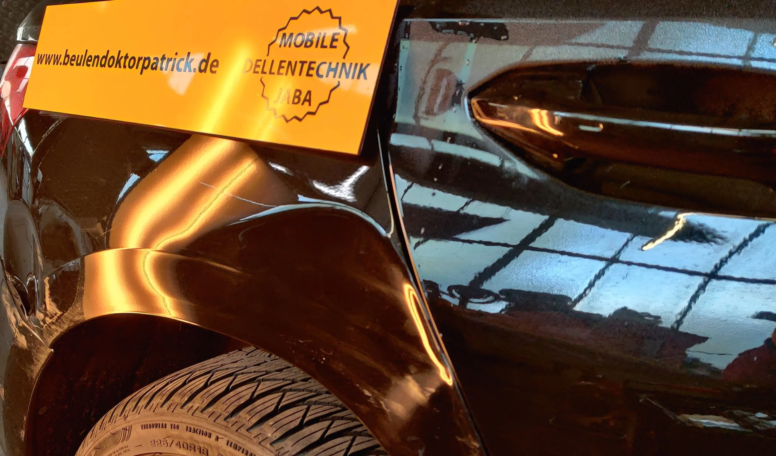 Nahaufnahme eines schwarzen Autos mit einem gelben Aufkleber, der die Webseite www.beulendoctorpatrick.de und den Begriff Mobiltechnik Jaba enthält.