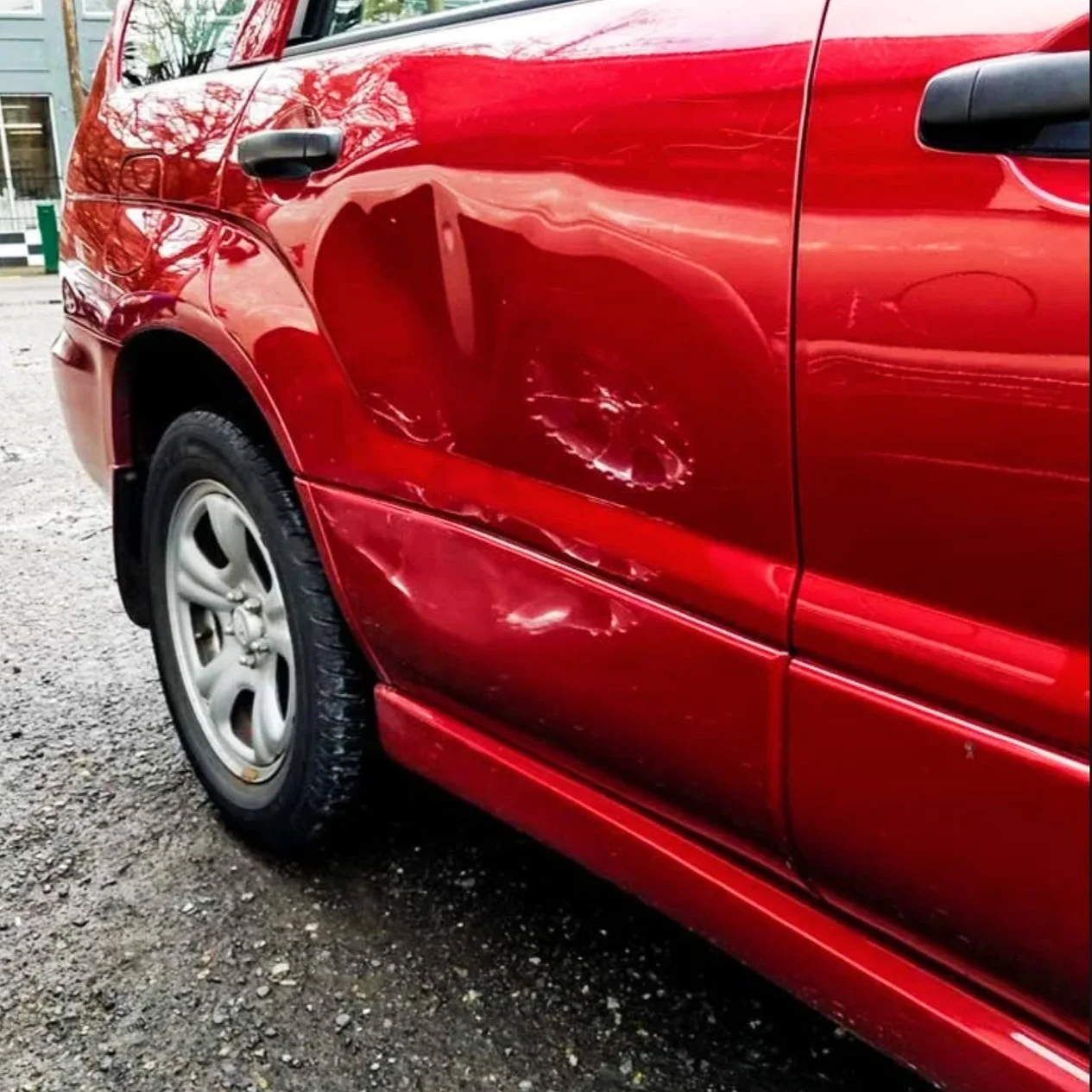 Ein rotes Auto mit Dellen und Kratzern an der Fahrerseite.