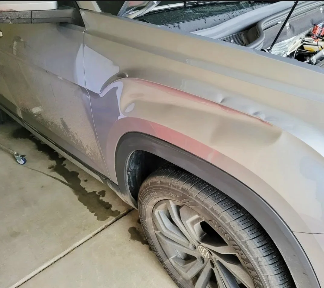 Nahaufnahme eines schwarzen VW-Autos mit beschädigter Seite, Reifen und abgelegtem Werkzeug im Hintergrund.