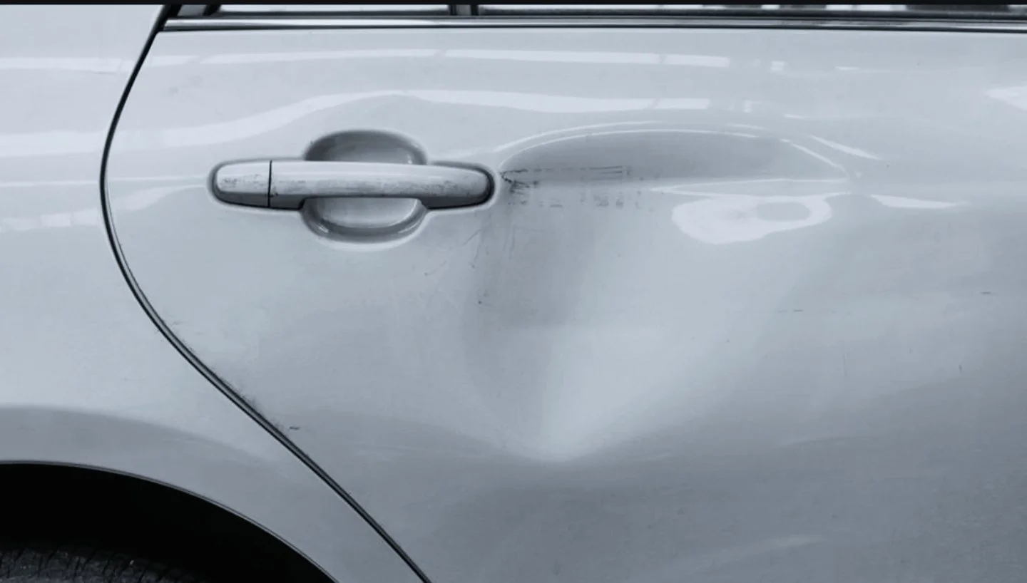 Nahaufnahme eines beschädigten silbernen Autotürgriffs und Dellen an der Tür