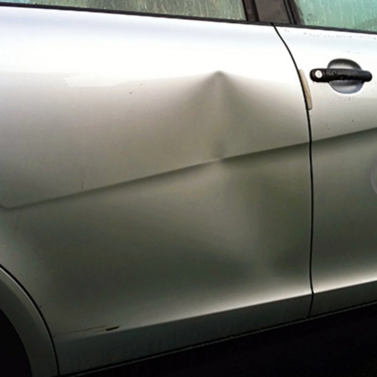 Ein silbernes Auto mit einer Delle an der Fahrertür auf der linken Seite.