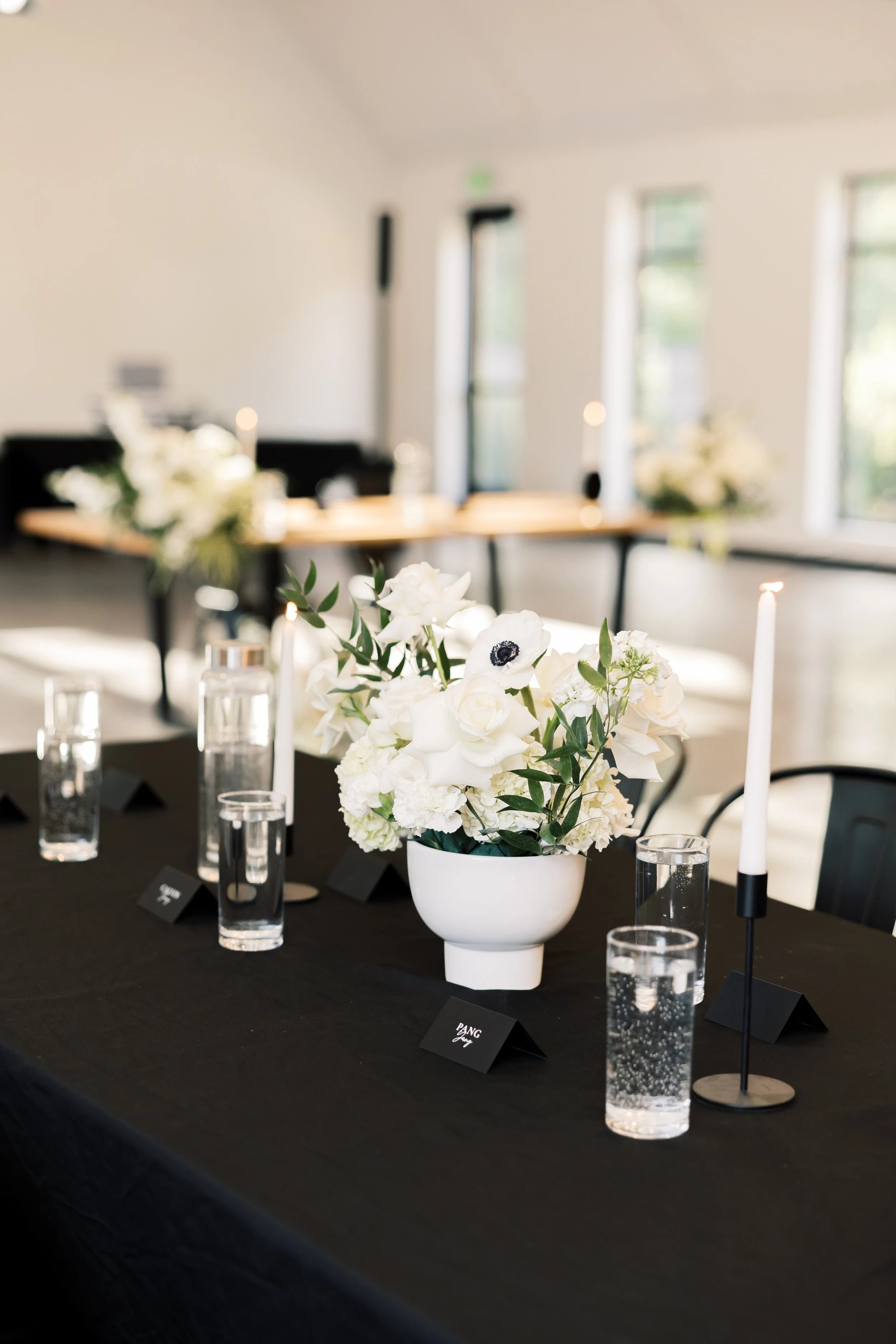 Table setting with a black tablecloth, white flower arrangement, and black velvet table numbers