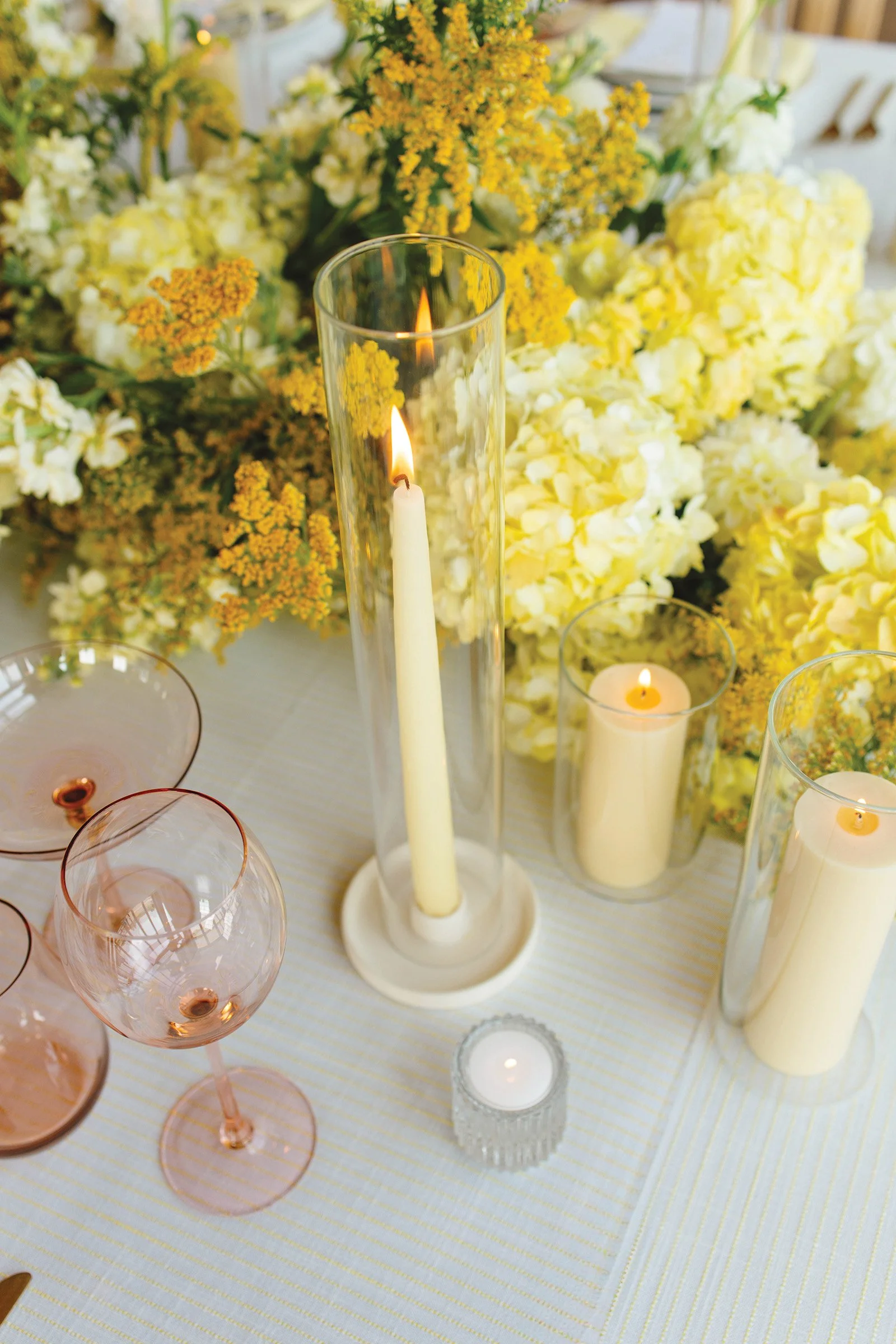 Place setting at a wedding reception table with yellow taper candles and blush pink glassware