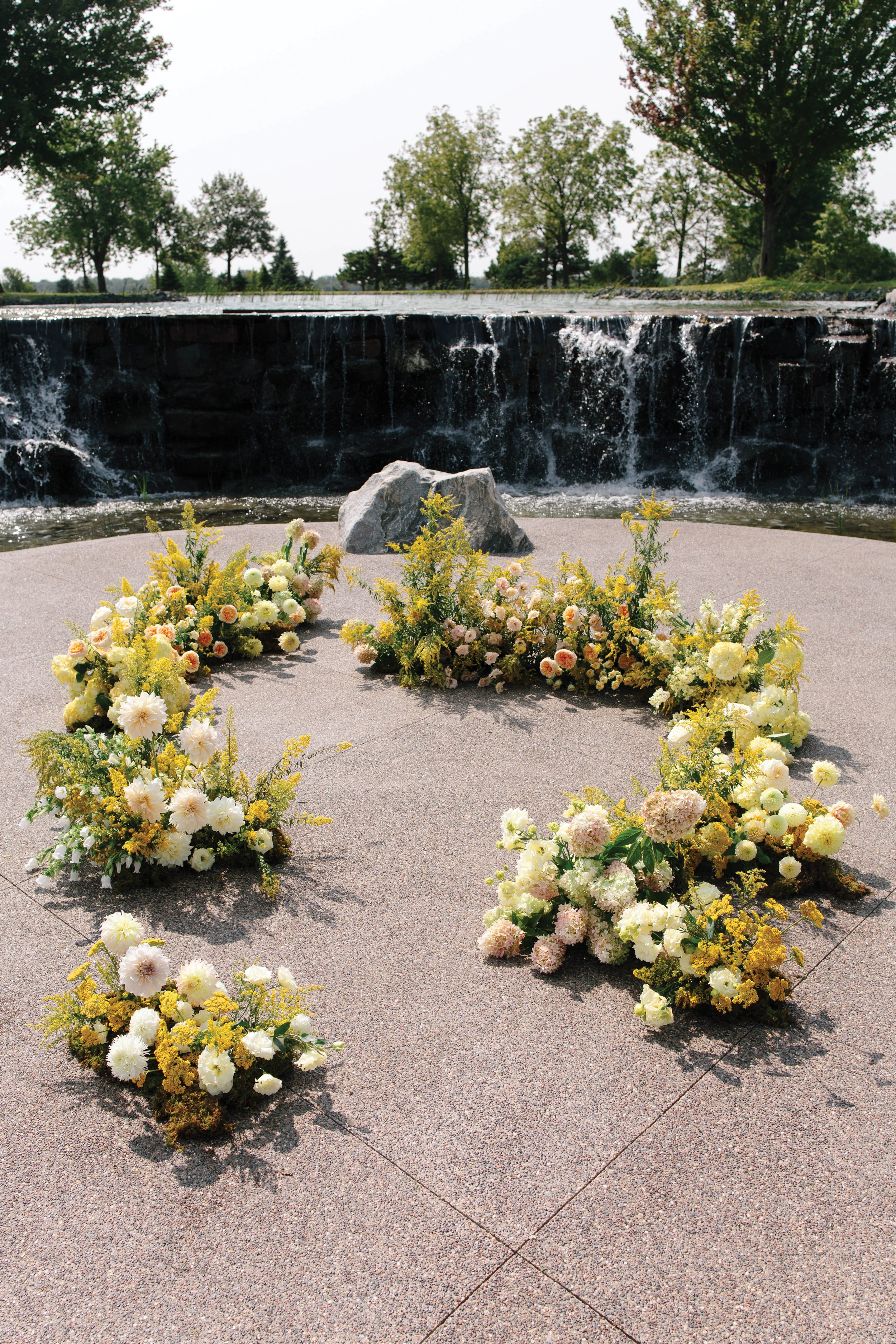 Yellow flowers arranged on the ground in front of a waterfall 