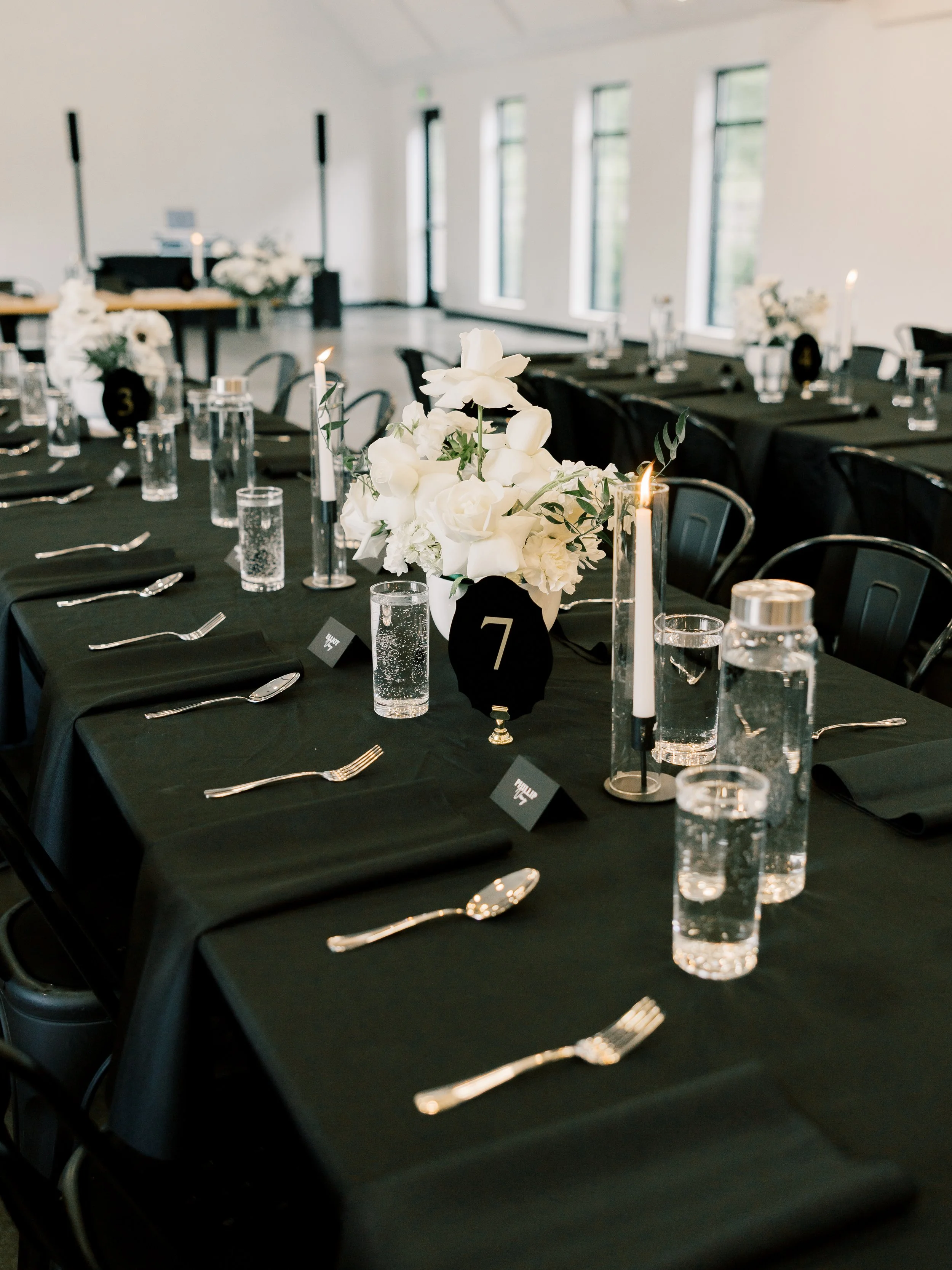 Table setting with a black tablecloth, white flower arrangement, and black velvet table numbers