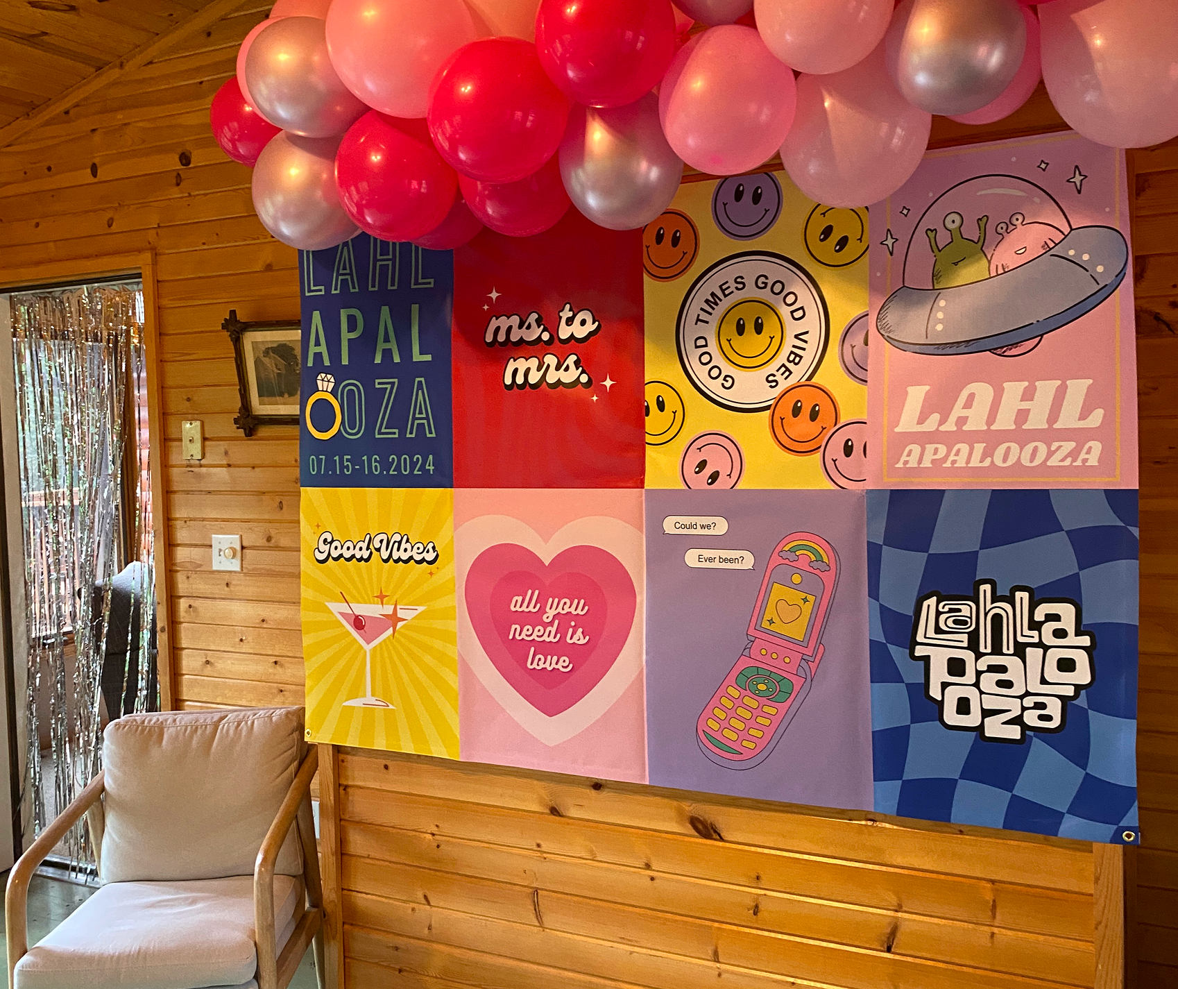 Decorative wall with colorful posters featuring smiley faces, a UFO with aliens, a phone with speech bubbles, and a love heart, topped with pink and red balloons.