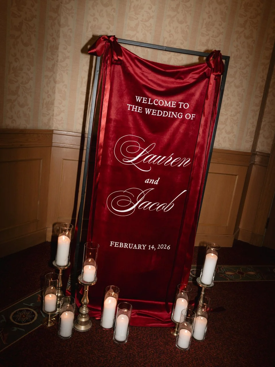 Red velvet welcome sign hanging on a black stand with lit candles around the base