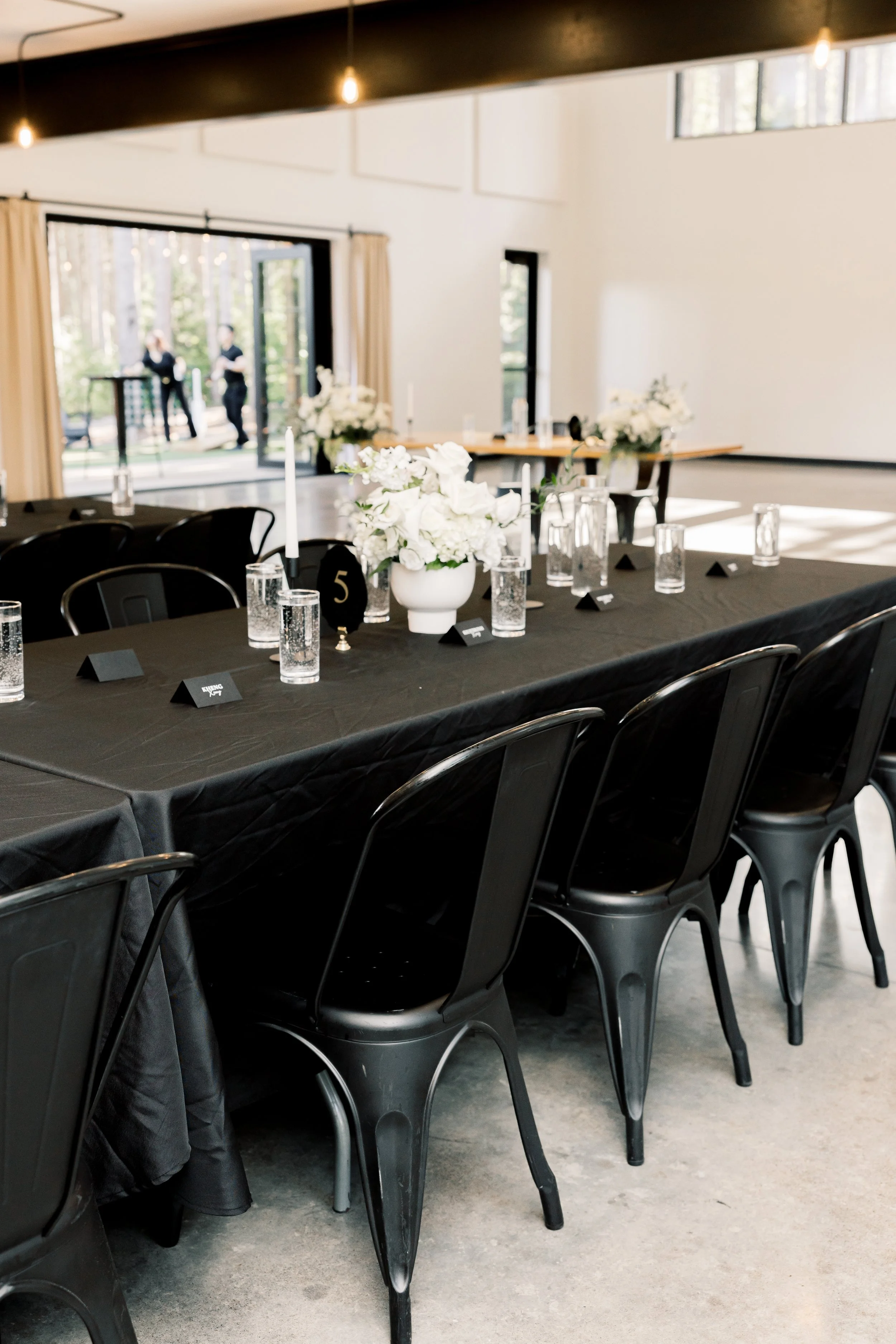 Table setting with a black tablecloth, white flower arrangement, and black velvet table numbers