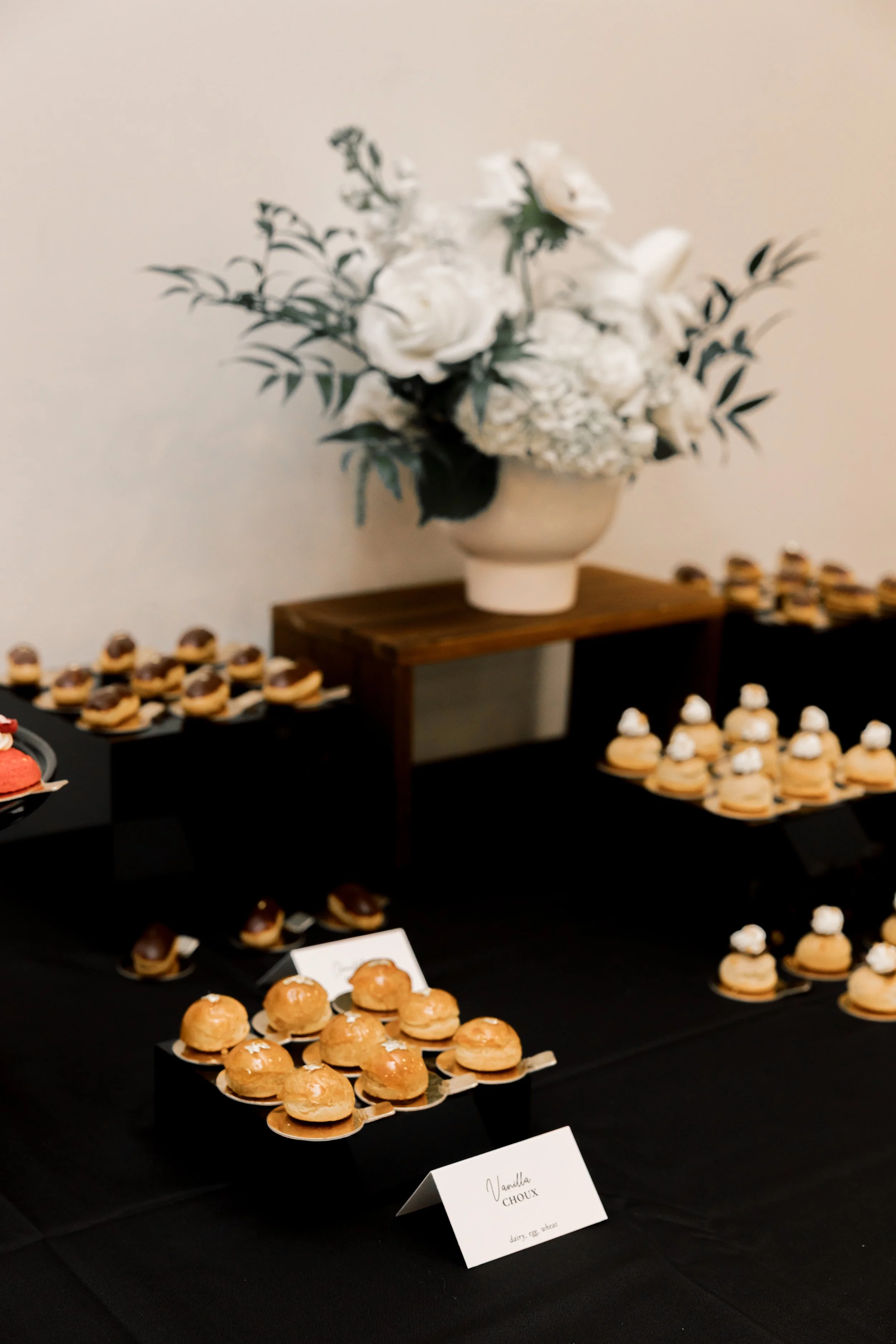 An assortment of puff pastries on a black tablecloth with a white floral arrangement
