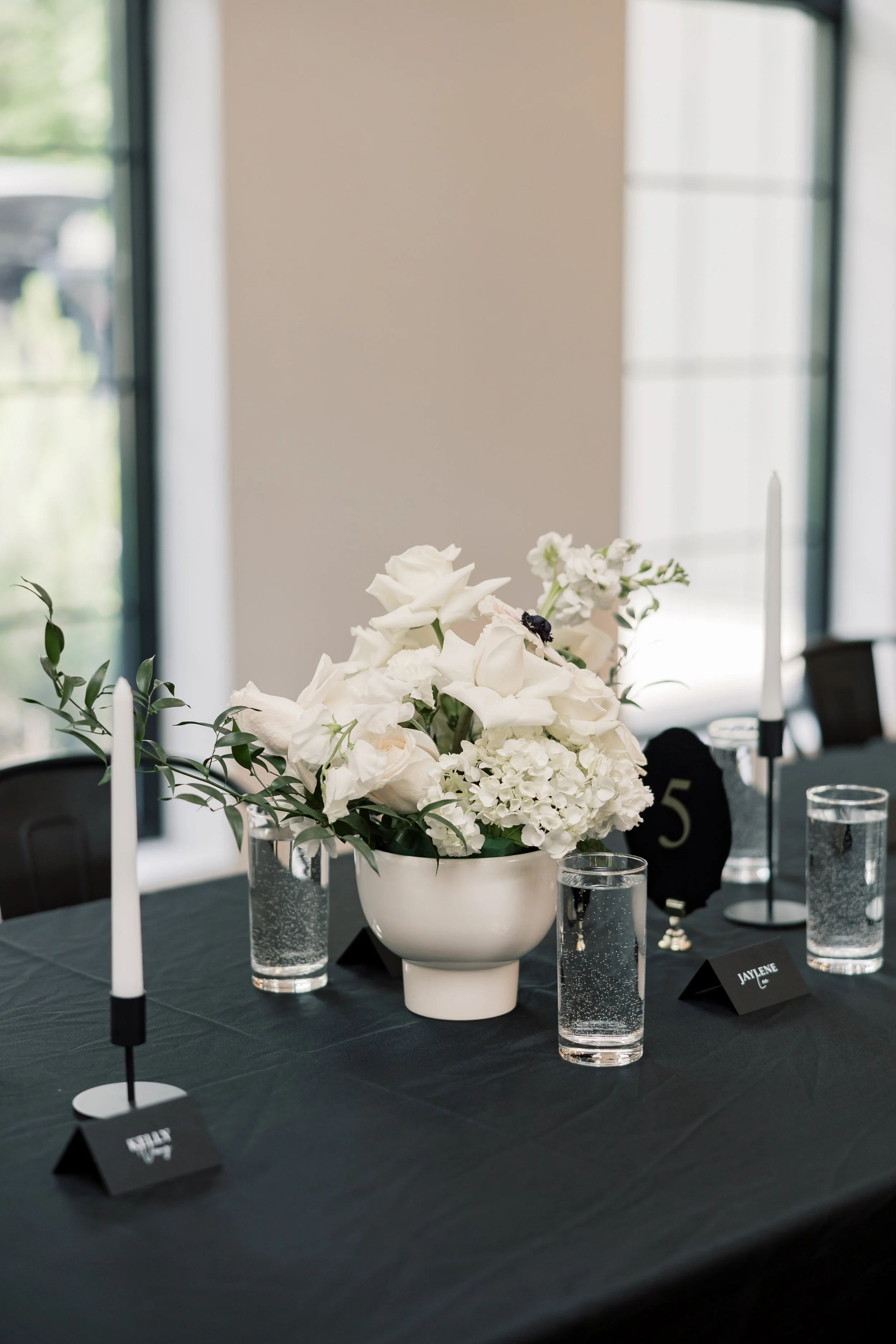 Table setting with a black tablecloth, white flower arrangement, and black velvet table numbers