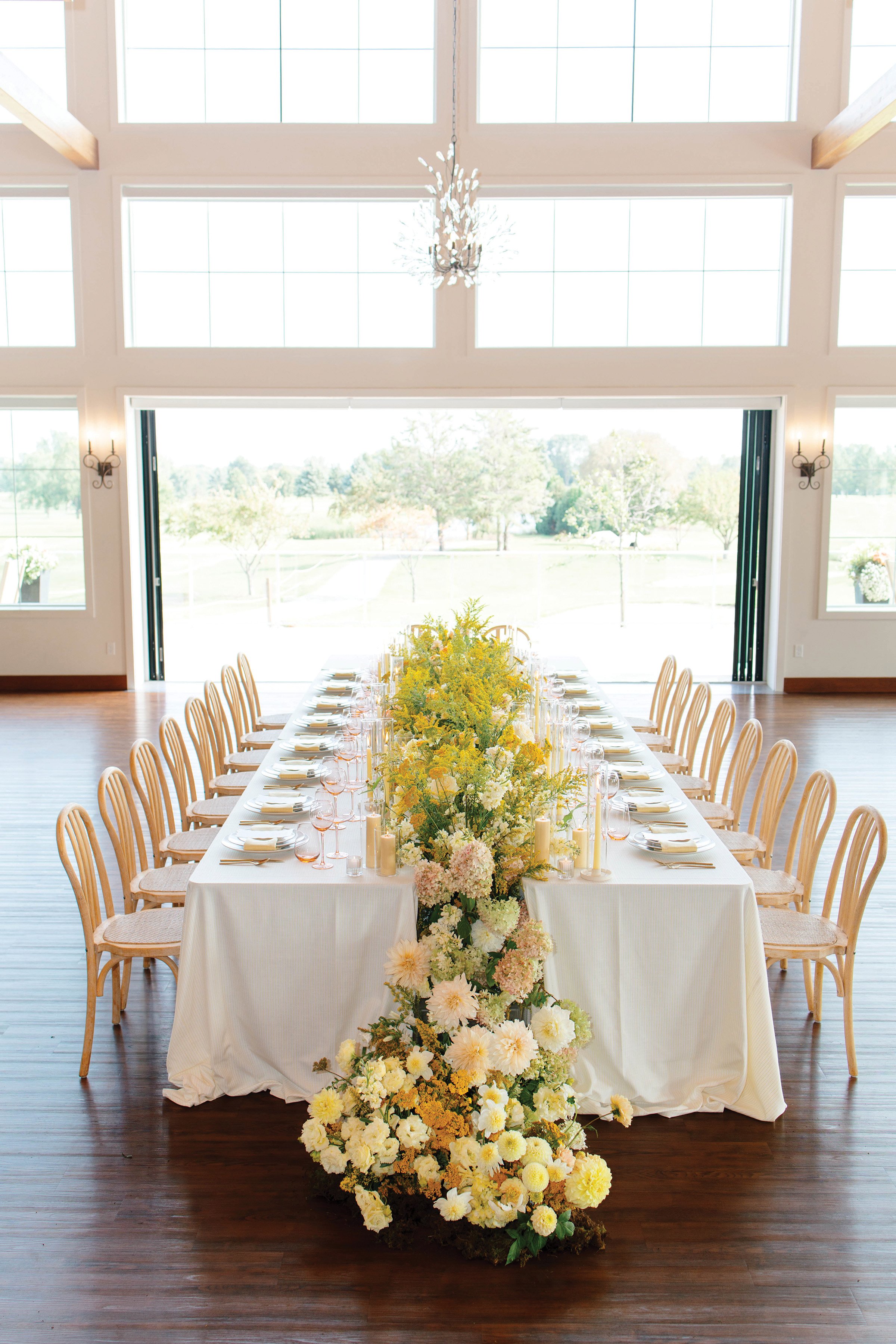 Wedding reception head table with a row of yellow flowers emerging down the center and overflowing onto the ground 