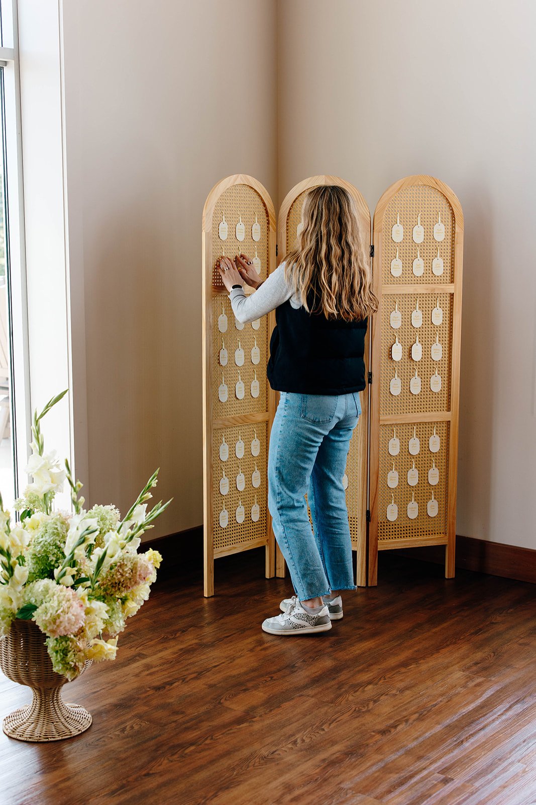 A woman placing escort cards on a rattan trifold privacy screen.