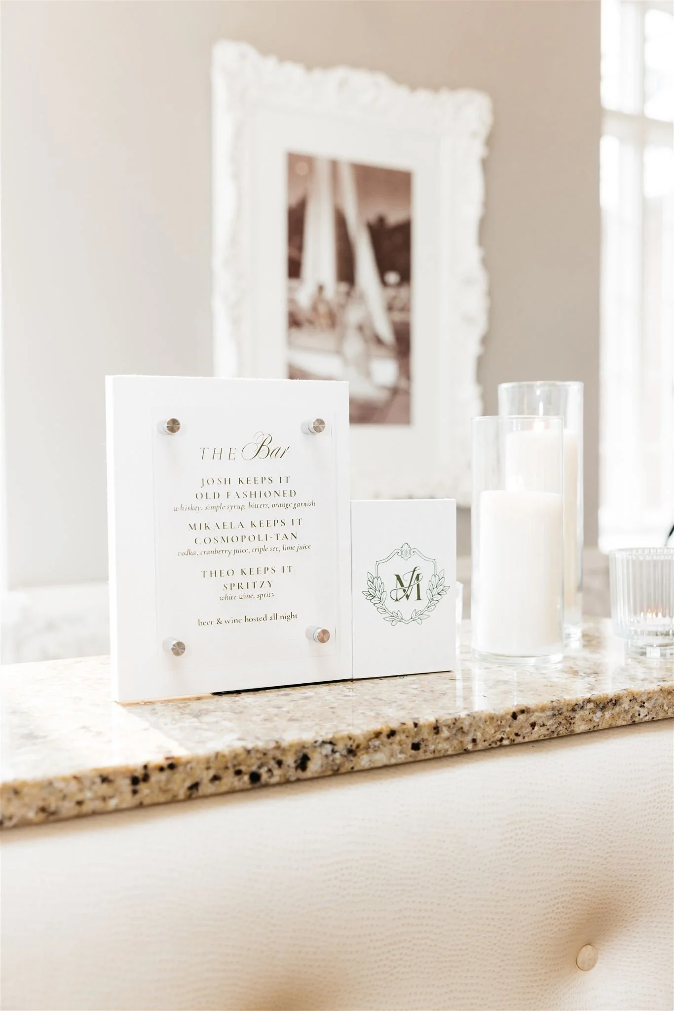 A white bar menu on a granite counter that has drink names and a custom wedding crest in green text.