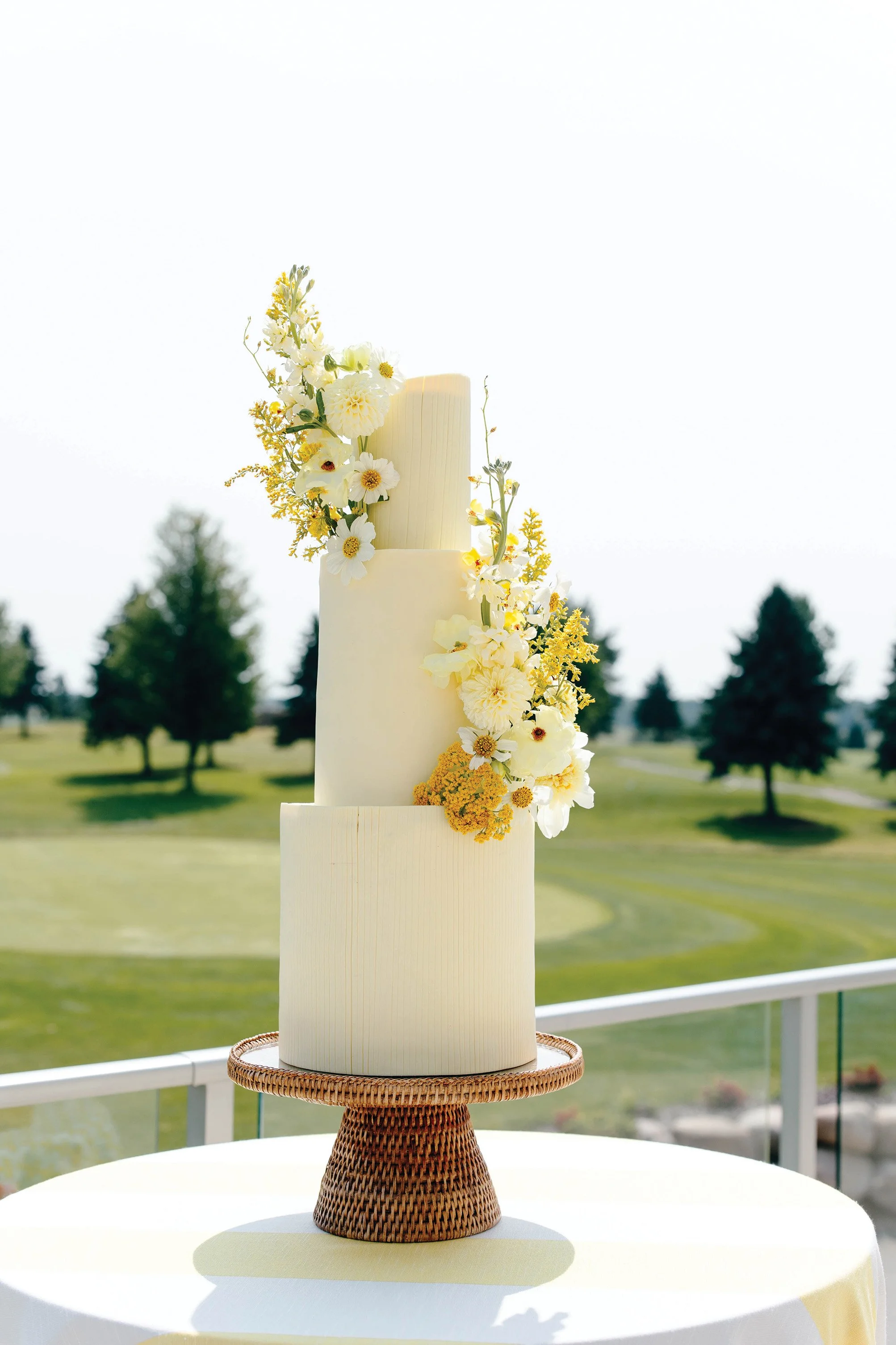A three tier wedding cake with pastel yellow frosting and flowers