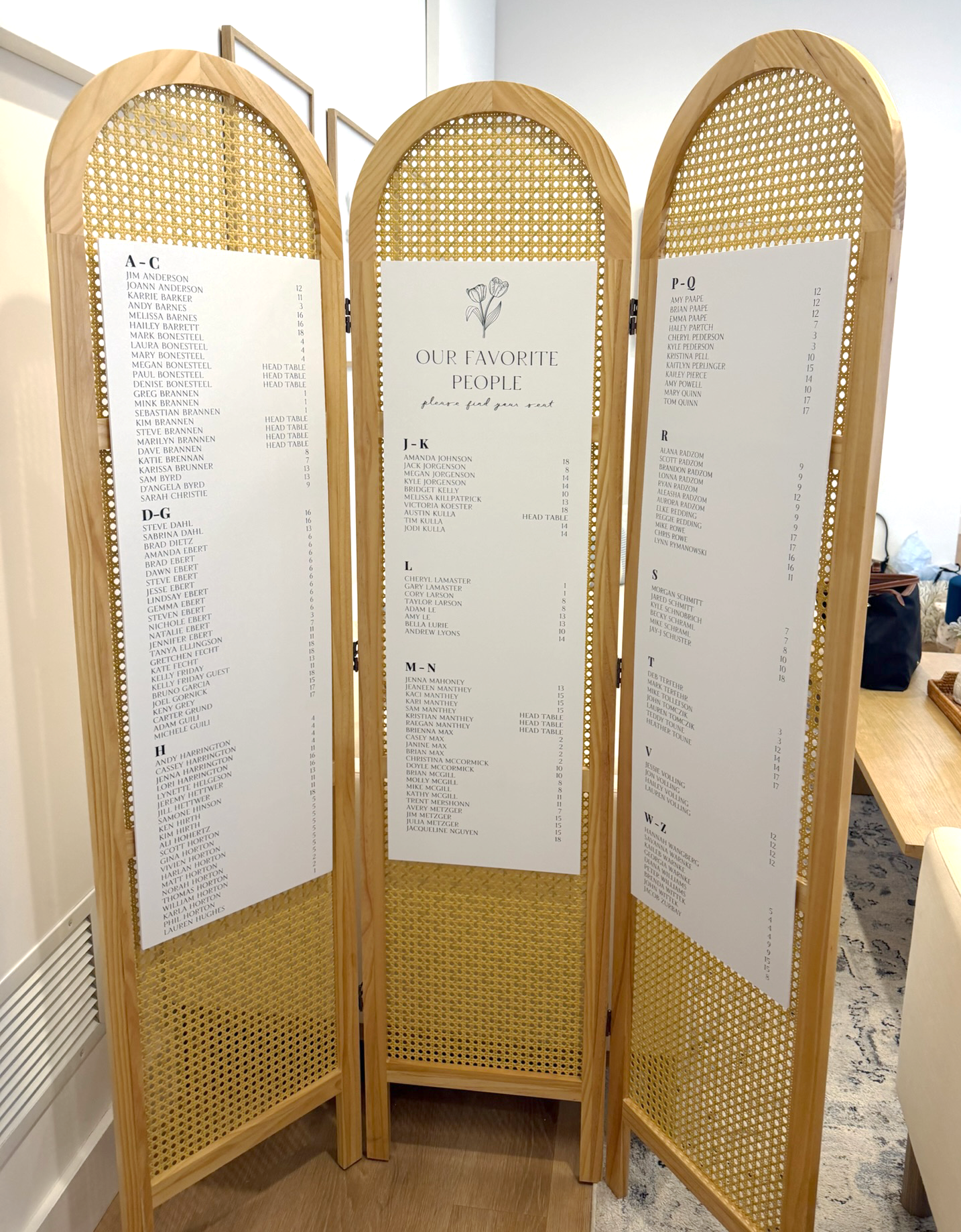 Rattan divider with three white seating chart poster board panels.