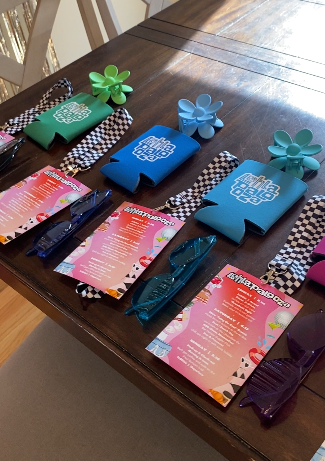 Colorful koozies and printed event itinerary cards laying on a table with colorful sunglasses.
