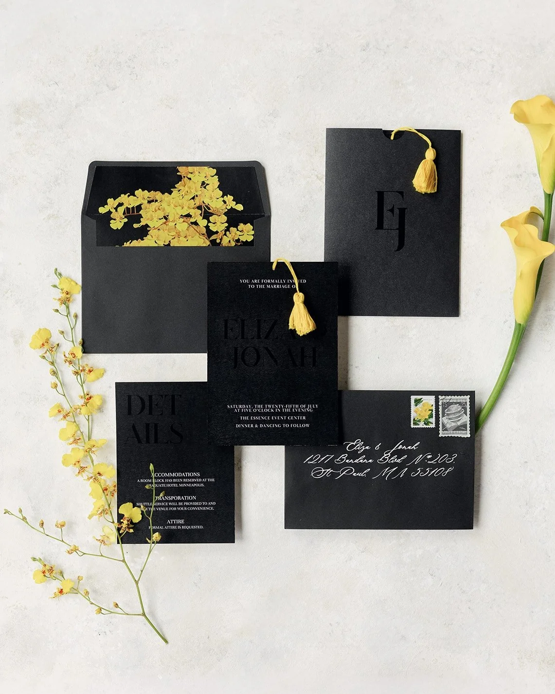 Black and yellow wedding invitation flatlay including a yellow floral envelope liner and yellow invitation tassel surrounded by yellow flowers.