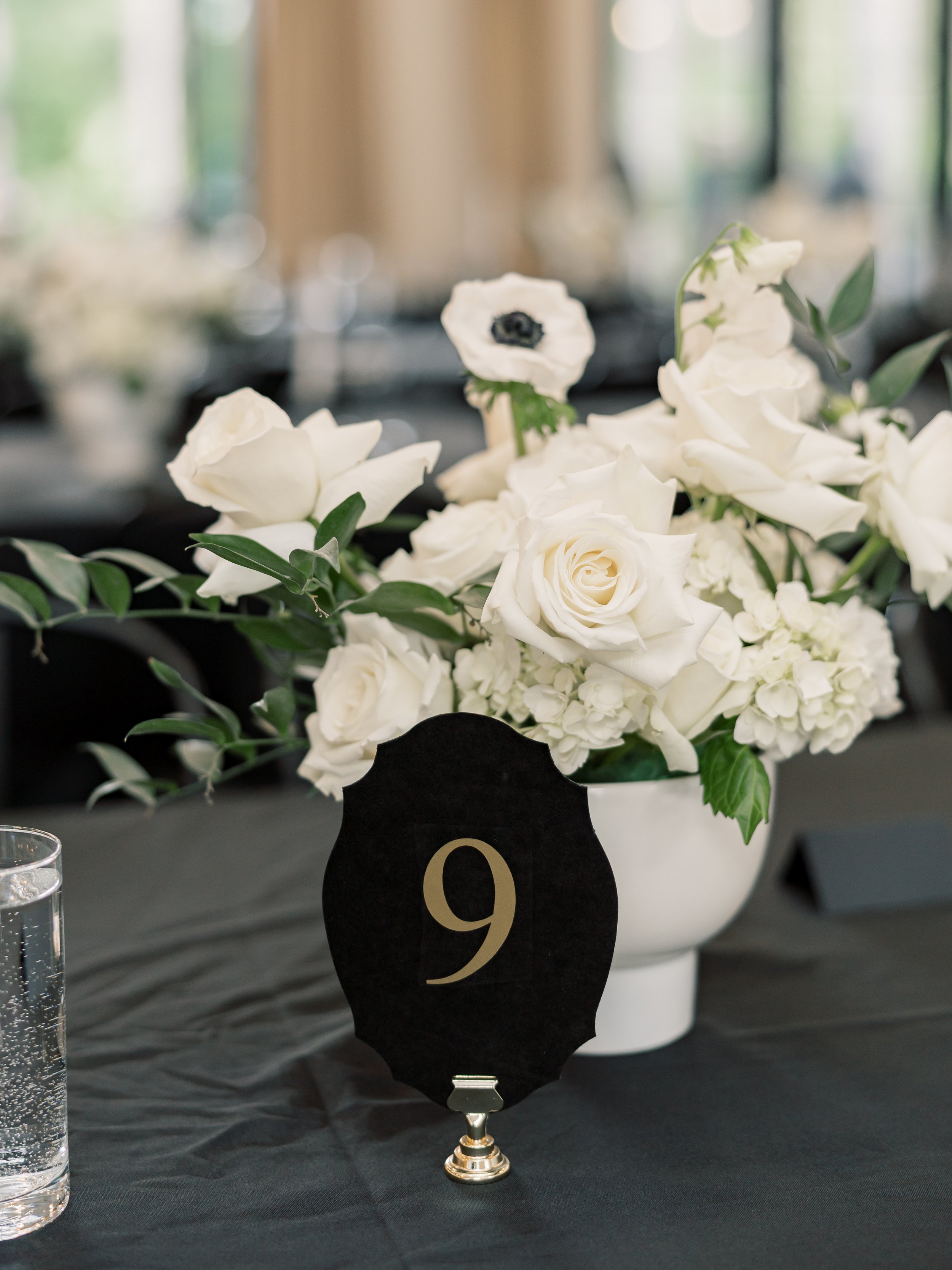 Table setting with a black tablecloth, white flower arrangement, and black velvet table numbers
