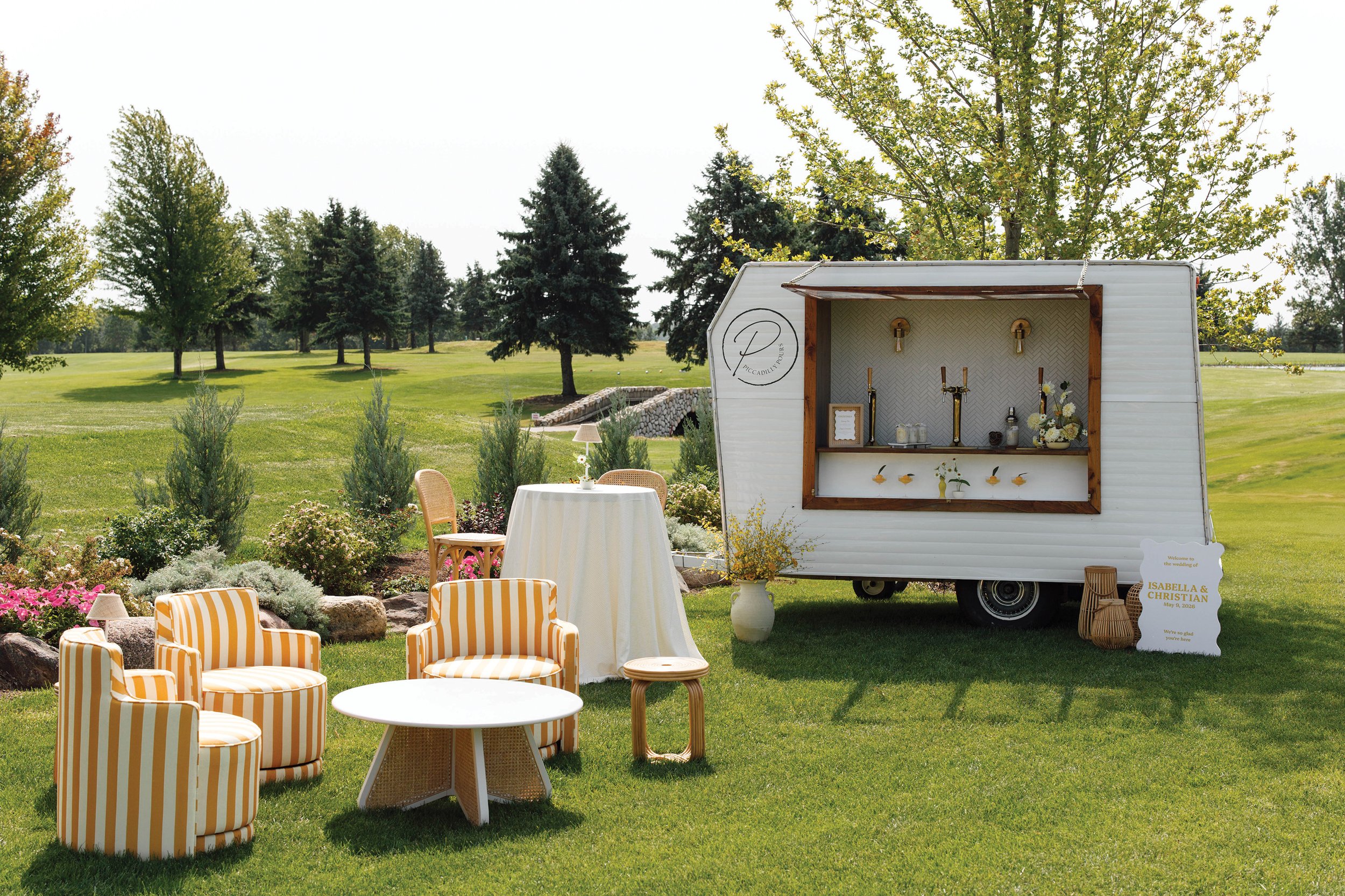 Outdoor seating arrangement with yellow striped chairs in front of a white bar camper