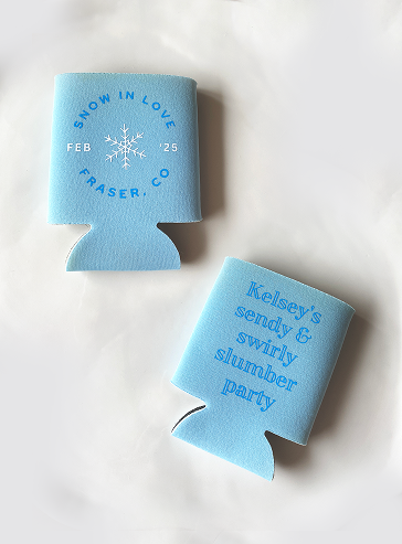 Two light blue beverage koozies with dark blue text, one reading 'SNOW IN LOVE FEB 25 FRASER, CO' and the other reading 'Kelsey's Sendy & Swirly Slumber Party' with a snowflake graphic.