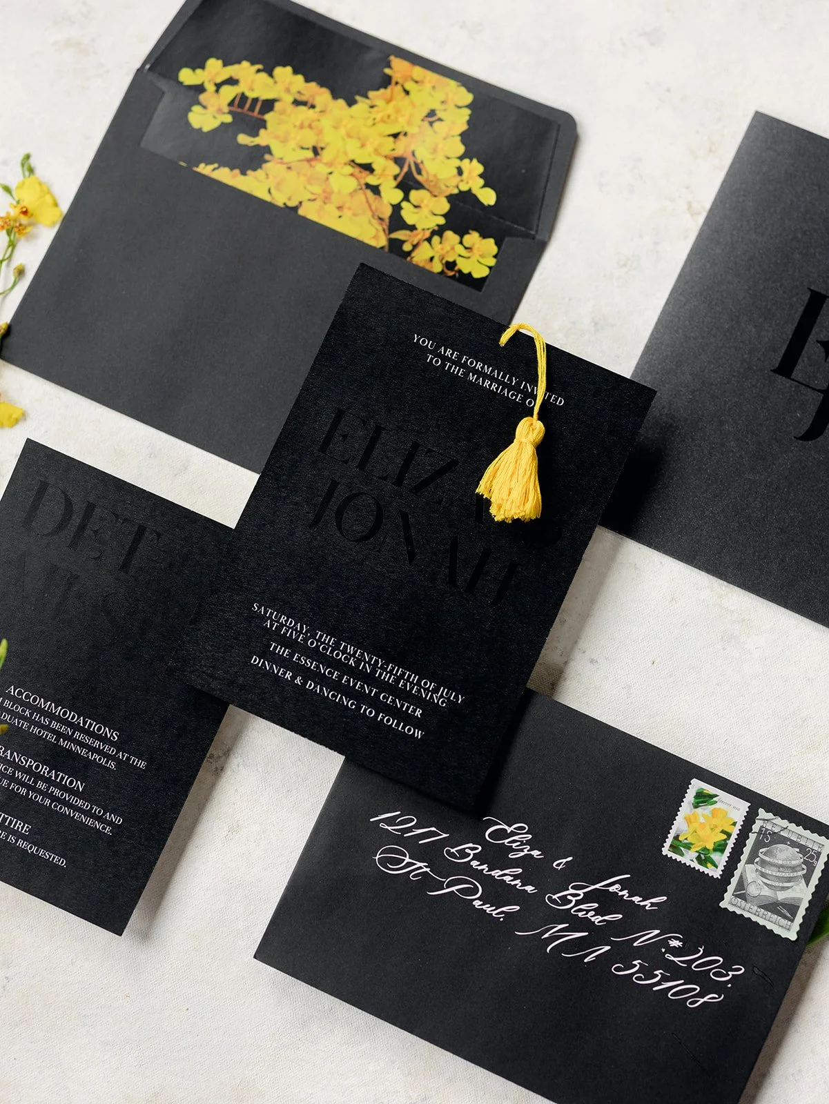 Black and yellow wedding invitation flatlay including a yellow floral envelope liner and yellow invitation tassel. 
