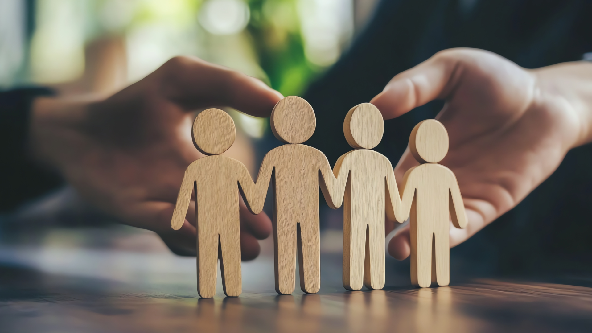 Hands holding wooden figurines of four people, symbolizing family or community.
