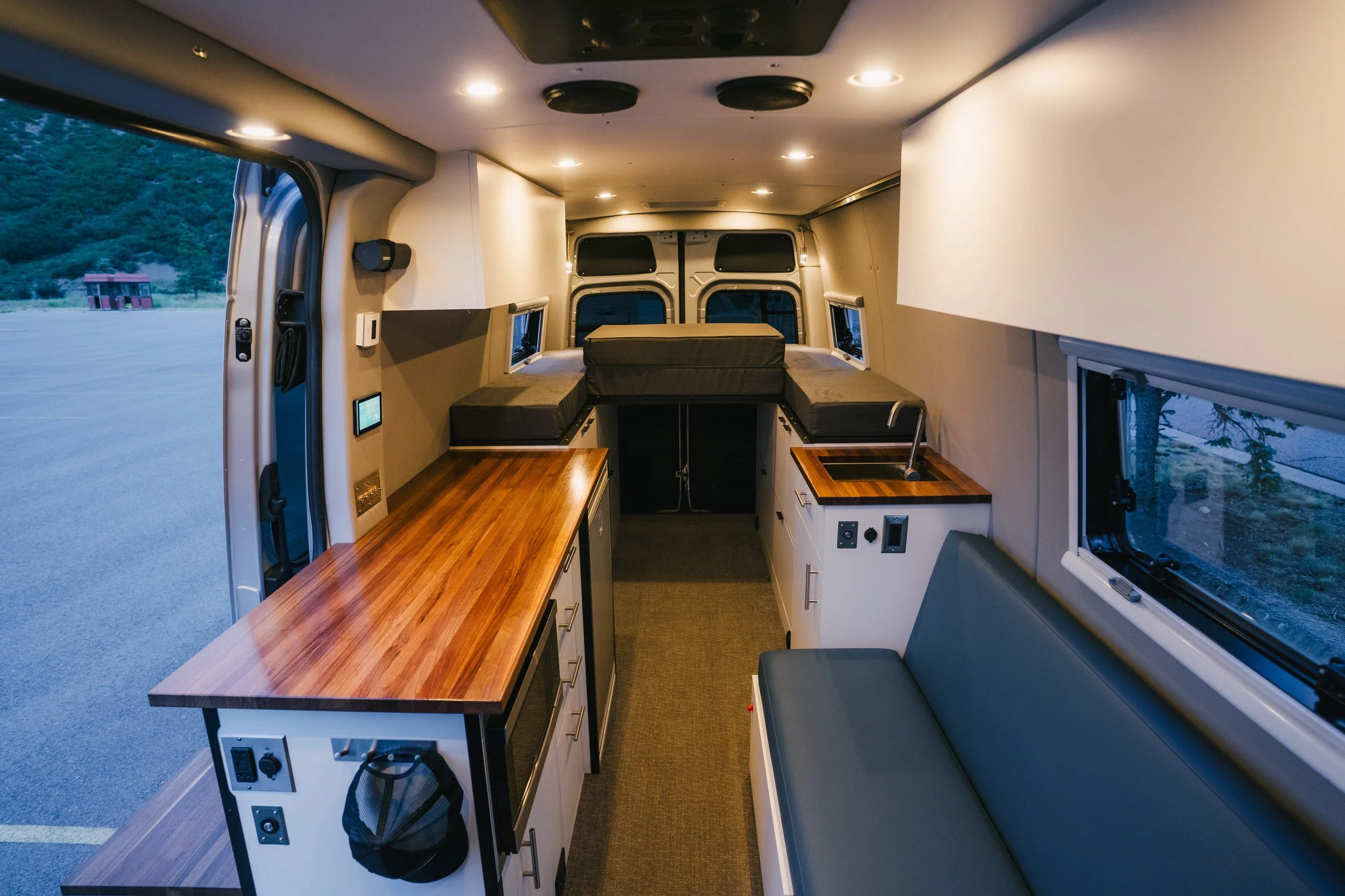 Interior of a converted van with built-in cabinets, a wooden counter, and a cushioned bench seat.