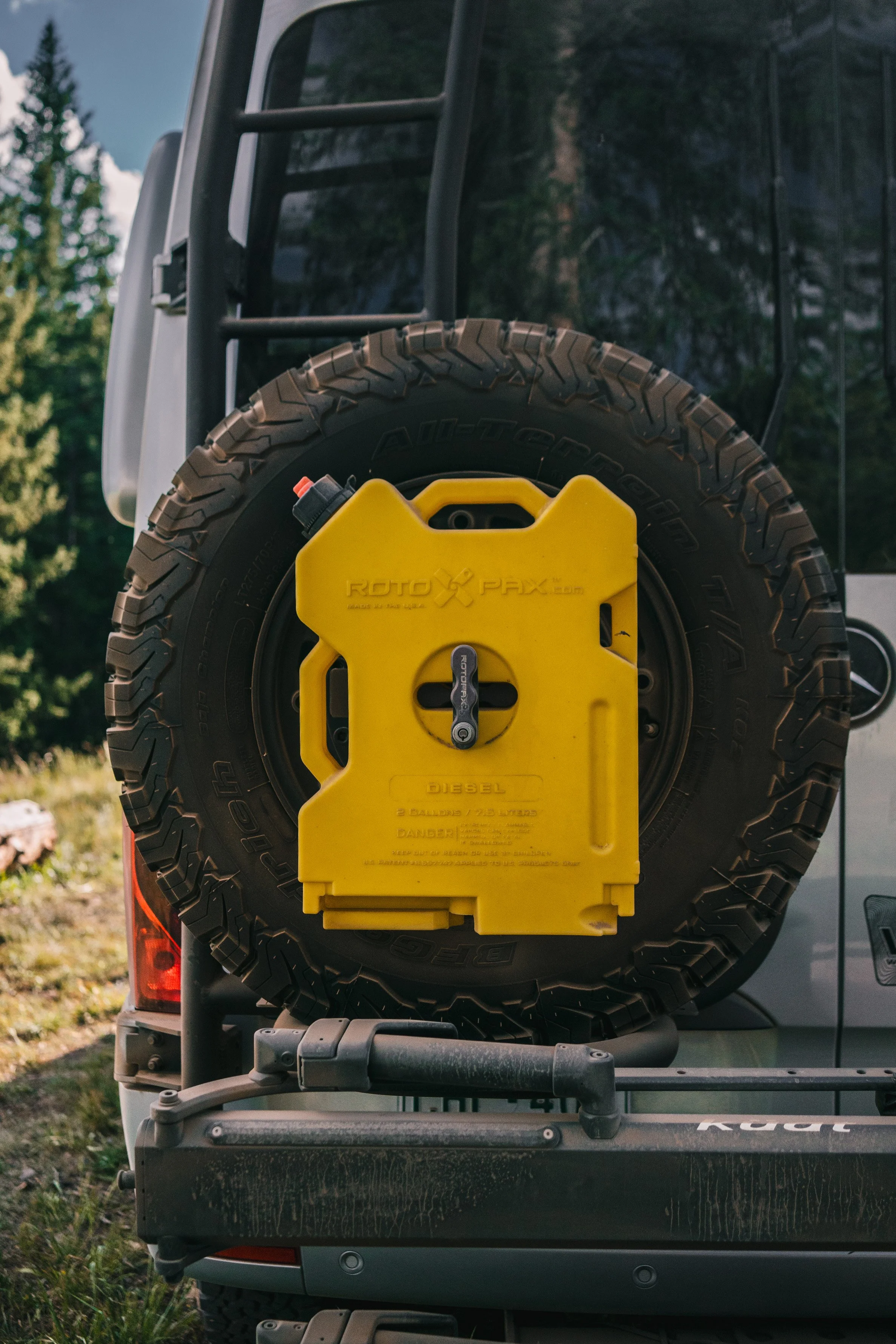 Back of a vehicle with a spare tire mounted, secured with a yellow lock box.