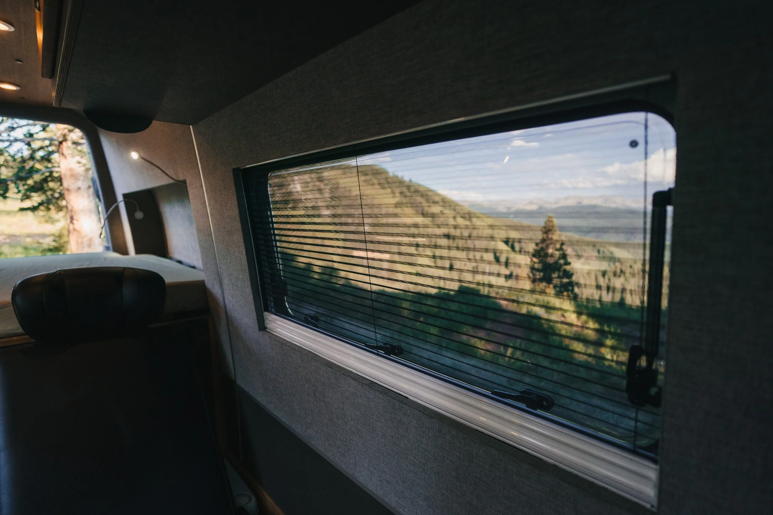Interior of a vehicle with a large window showing a hilly landscape with trees and mountains.