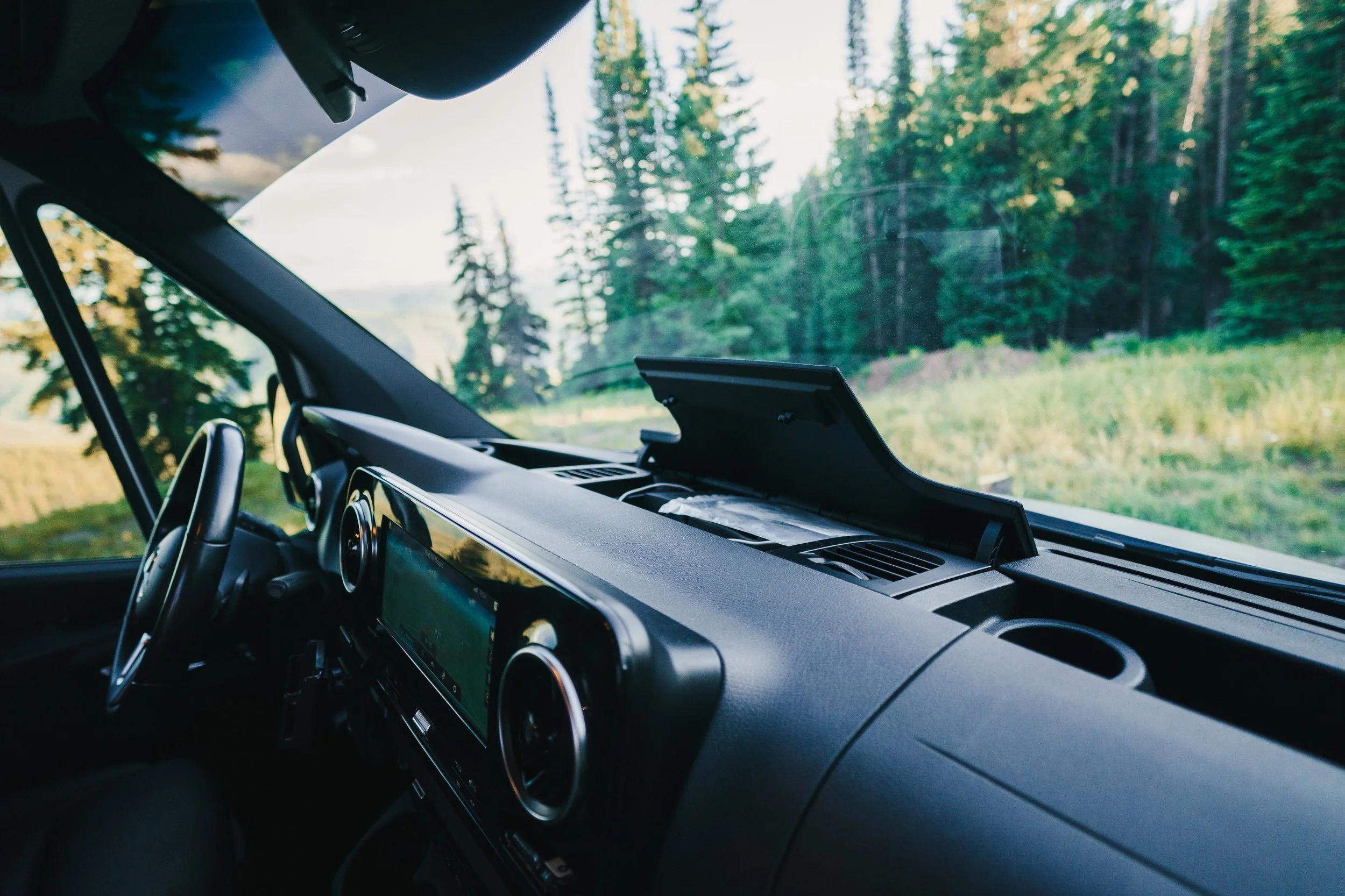 View of a vehicle's dashboard and steering wheel with a scenic forest landscape visible through the windshield.