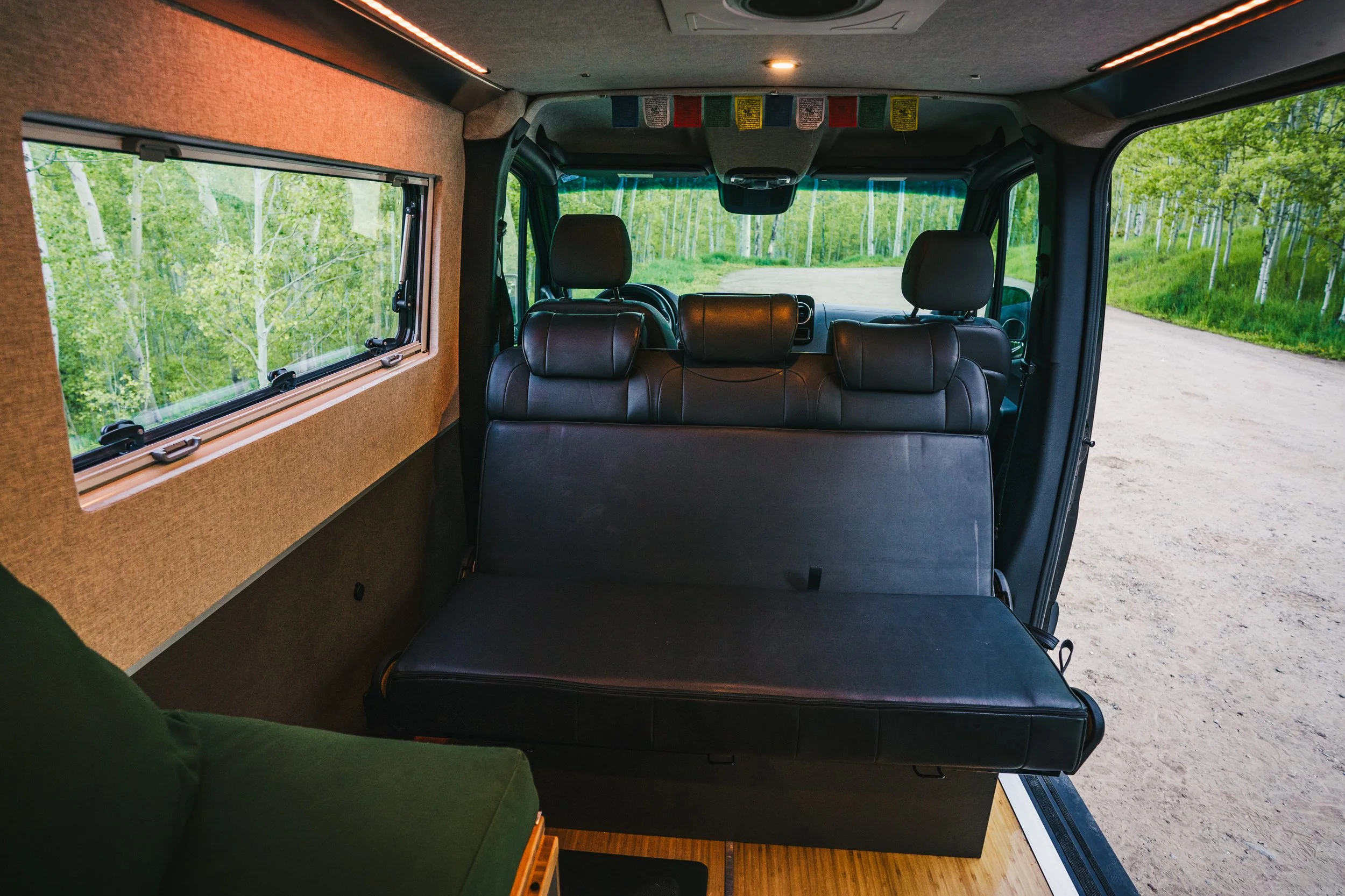 Interior of a van with black leather seats and a window showing green trees outside.