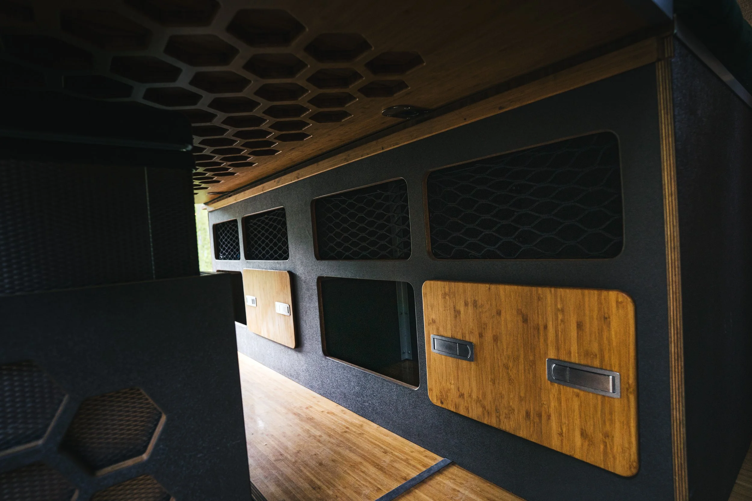 Modern conference room with black and wooden furniture, hexagonal ceiling design, and multiple storage compartments.