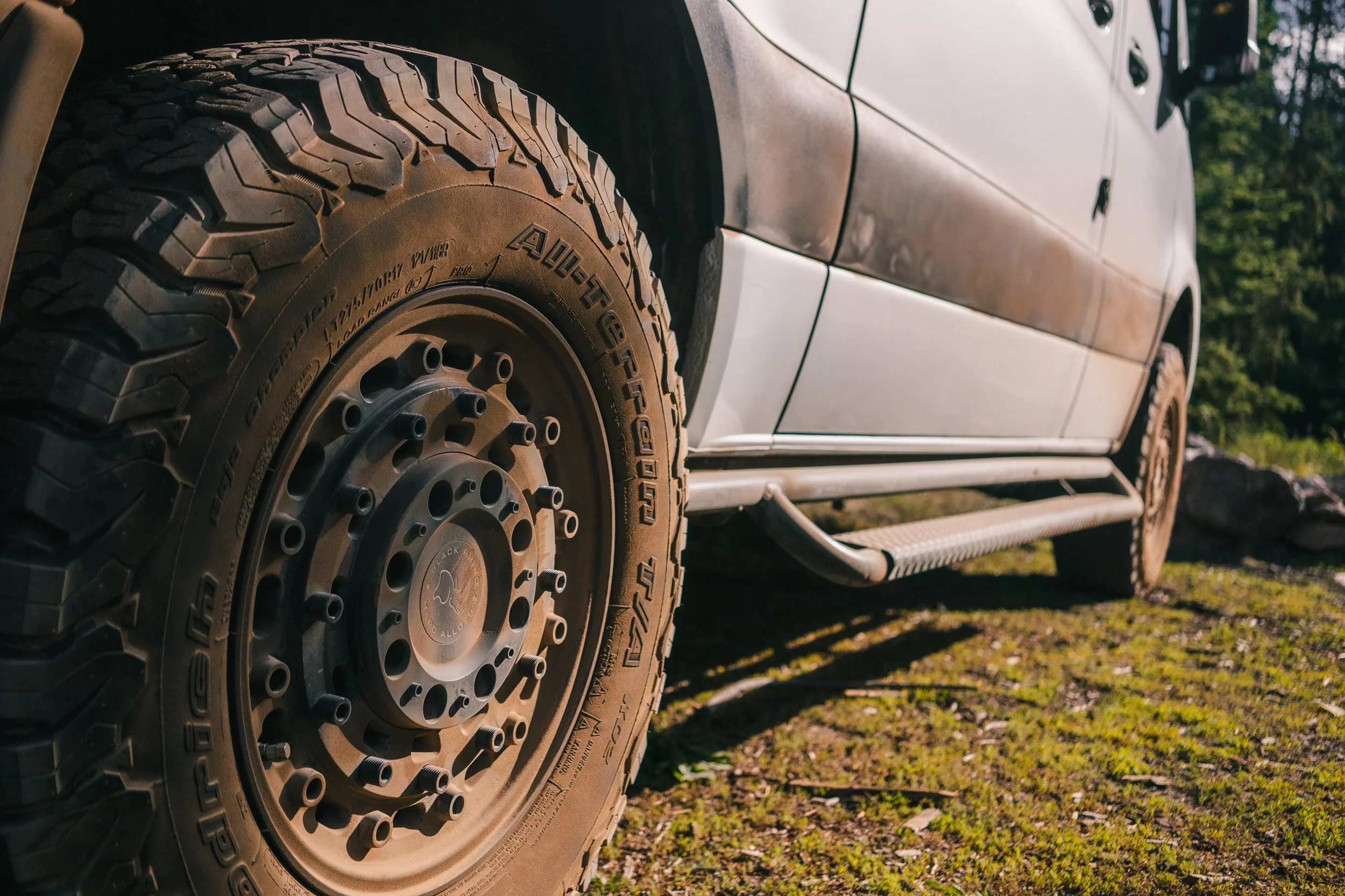 Close-up of a rugged off-road vehicle's tire with an aggressive tread pattern, parked on a grassy terrain.