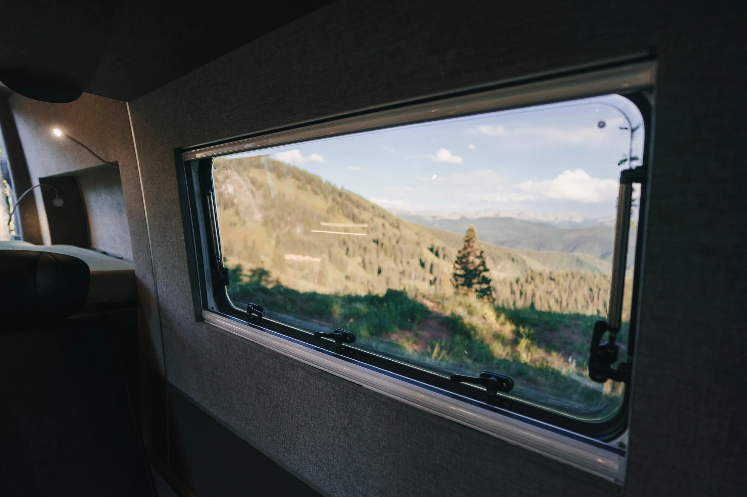 View through a window showing a landscape of green hills, trees, and a partly cloudy sky.