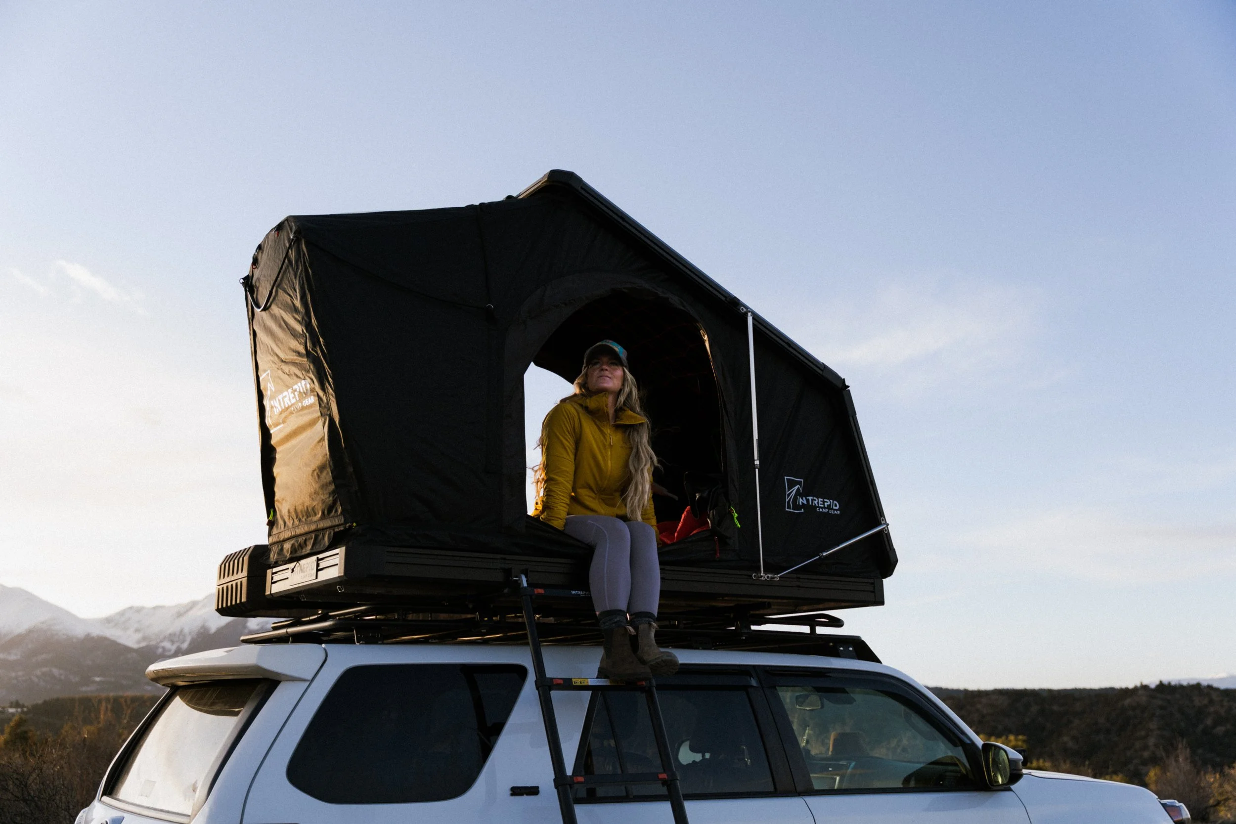 A woman sitting in a rooftop tent on top of a 4Runner looking off into the distance.