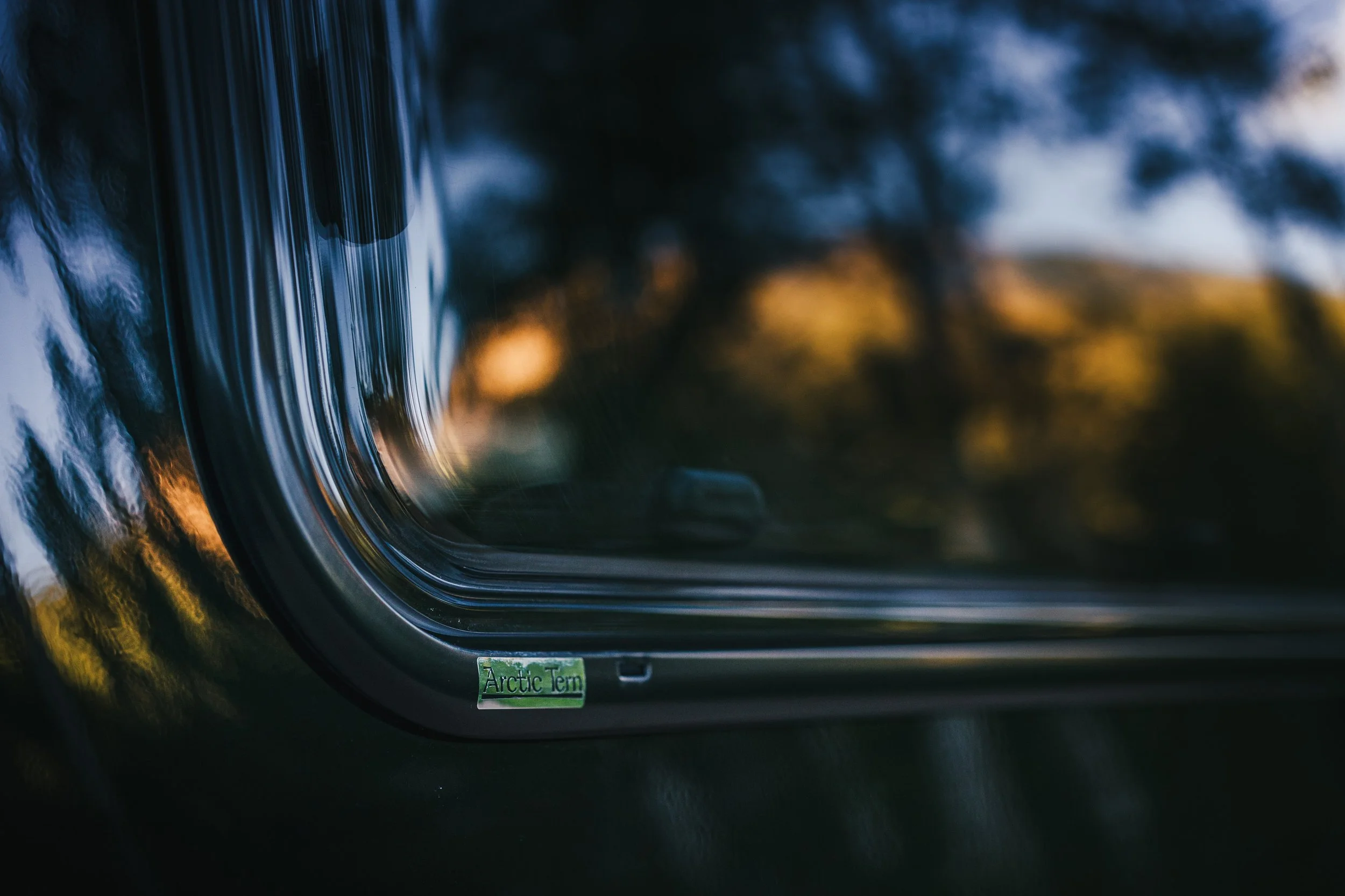 Close-up of a car window with a small green sticker that says 'Arctic Tern' at sunset or sunrise.