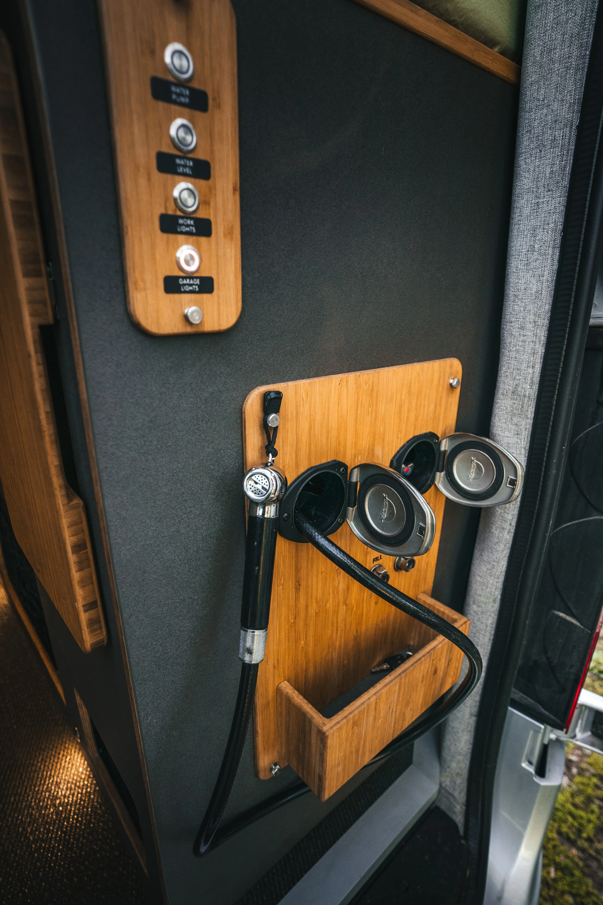 Panel with switches for interior vehicle controls, including water and garage lights, positioned next to a wooden board with a microphone, a pair of speakers, and a small storage compartment.