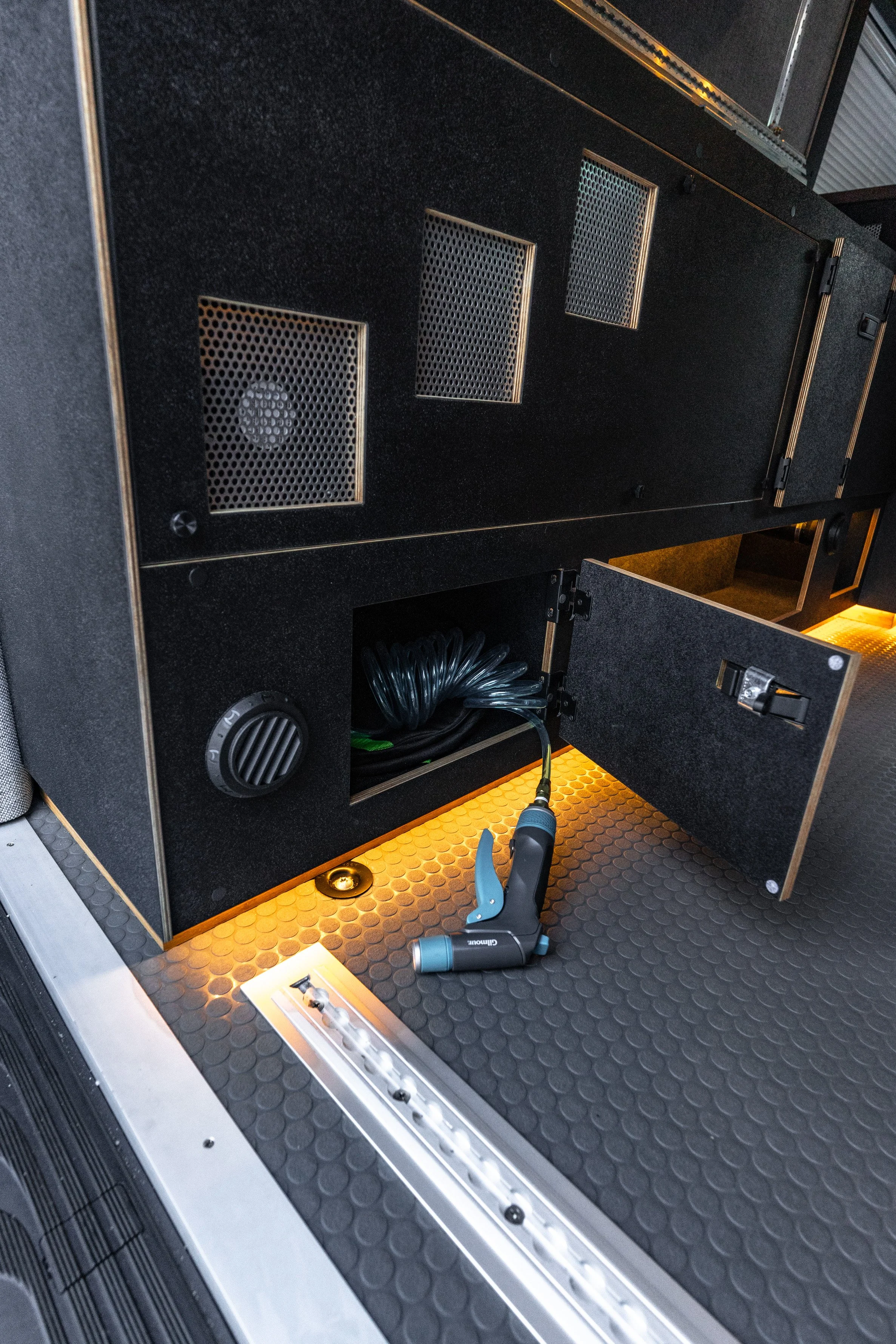 View of a black electrical cabinet with vents, open compartment with coiled cable, underfloor LED lighting, and a digital laser level on the floor.